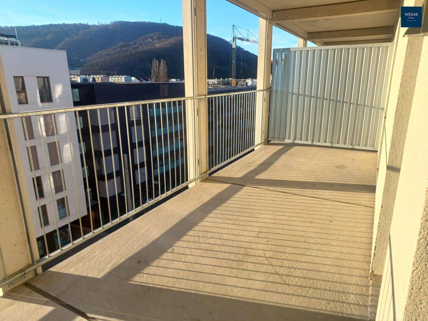 Heller Balkon mit Metallgeländer und Blick auf die umliegenden Gebäude und Berge.