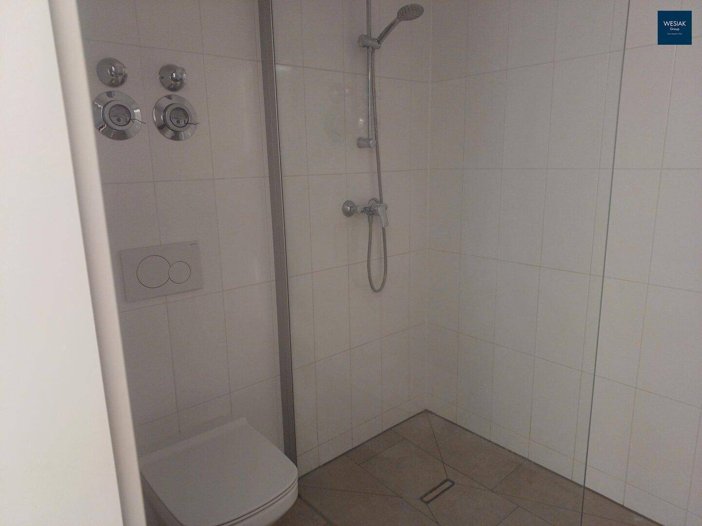 Helles Badezimmer mit Duschbereich, Glasabtrennung und wandhängendem WC, komplett gefliest.