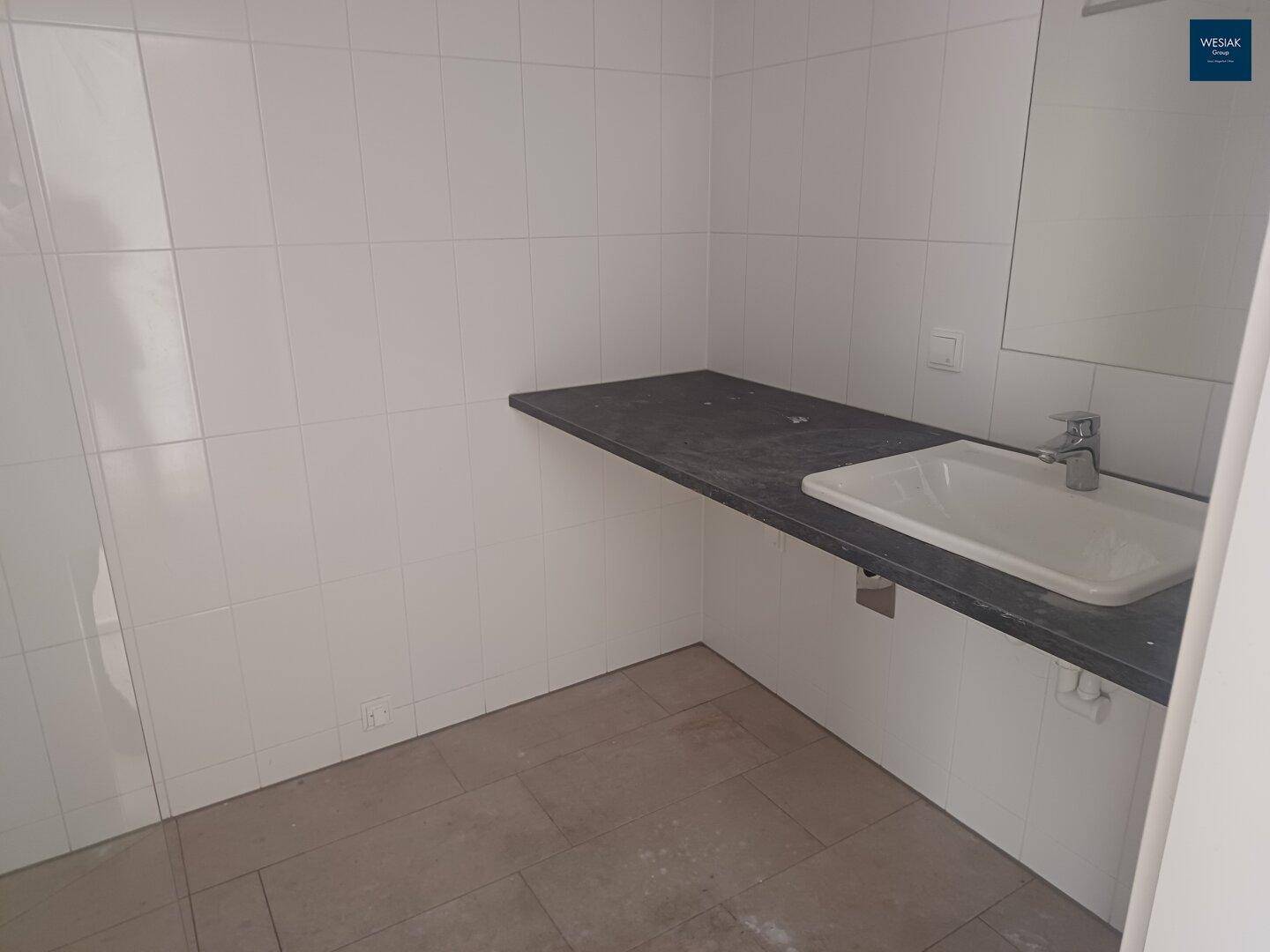Modernes Badezimmer mit weißen Fliesen, dunkler Ablage und einem einzelnen Waschbecken.