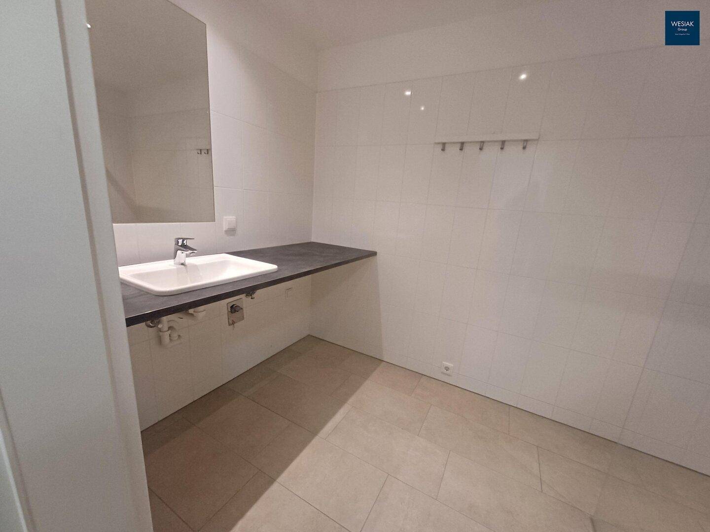 Geräumiges Badezimmer mit modernem Waschbecken, großem Spiegel und hellen Fliesen.