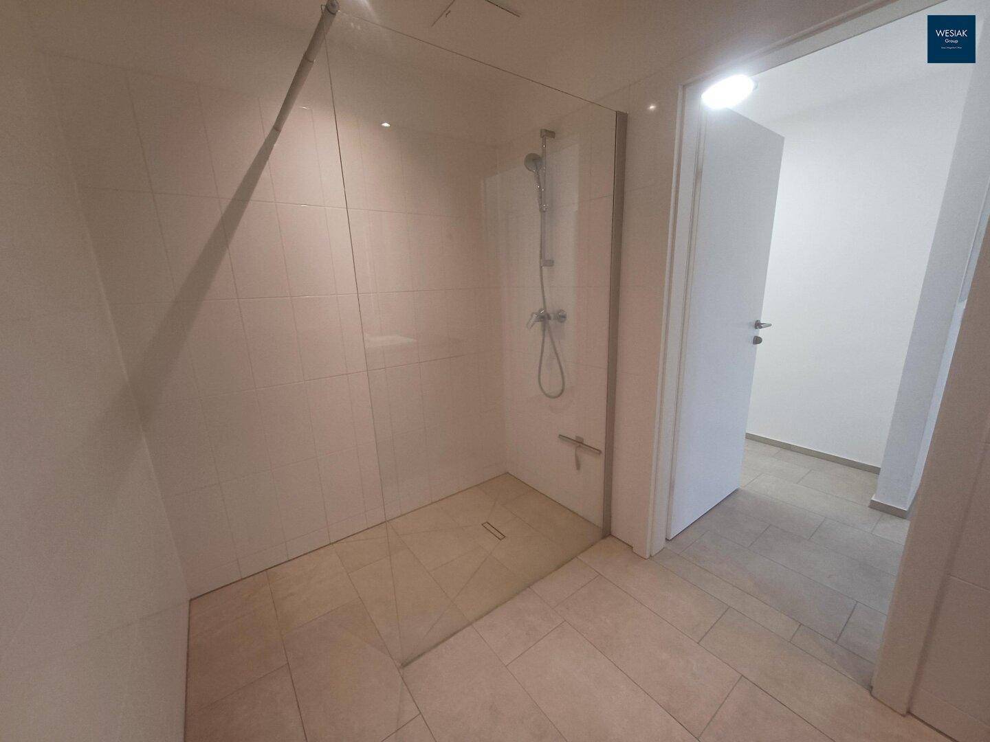 Modernes Badezimmer mit ebenerdiger Dusche und Glasabtrennung sowie hellen Fliesen.