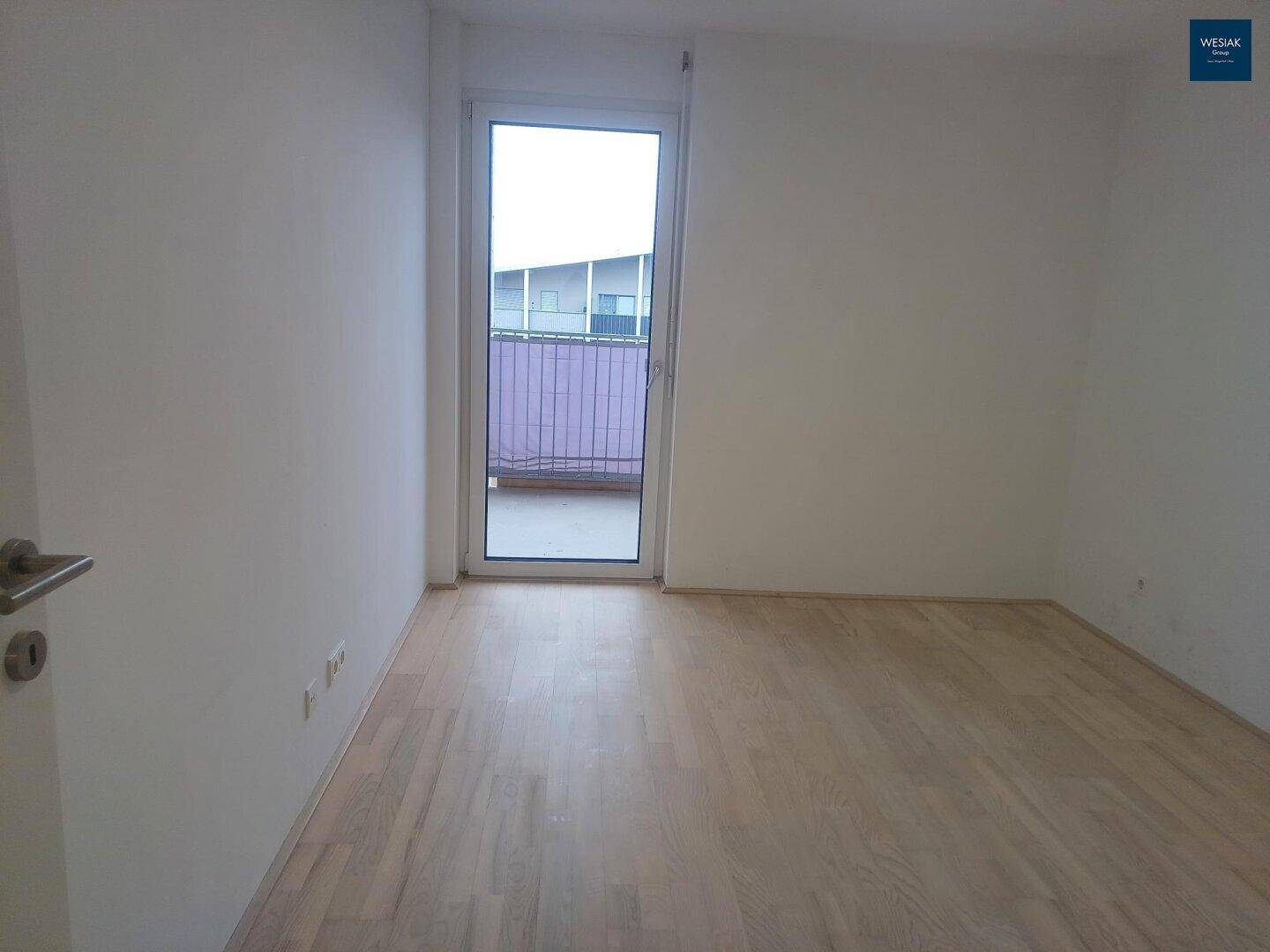 Lichtdurchflutetes Schlafzimmer mit Parkettboden und großem Fenster zum Balkon.