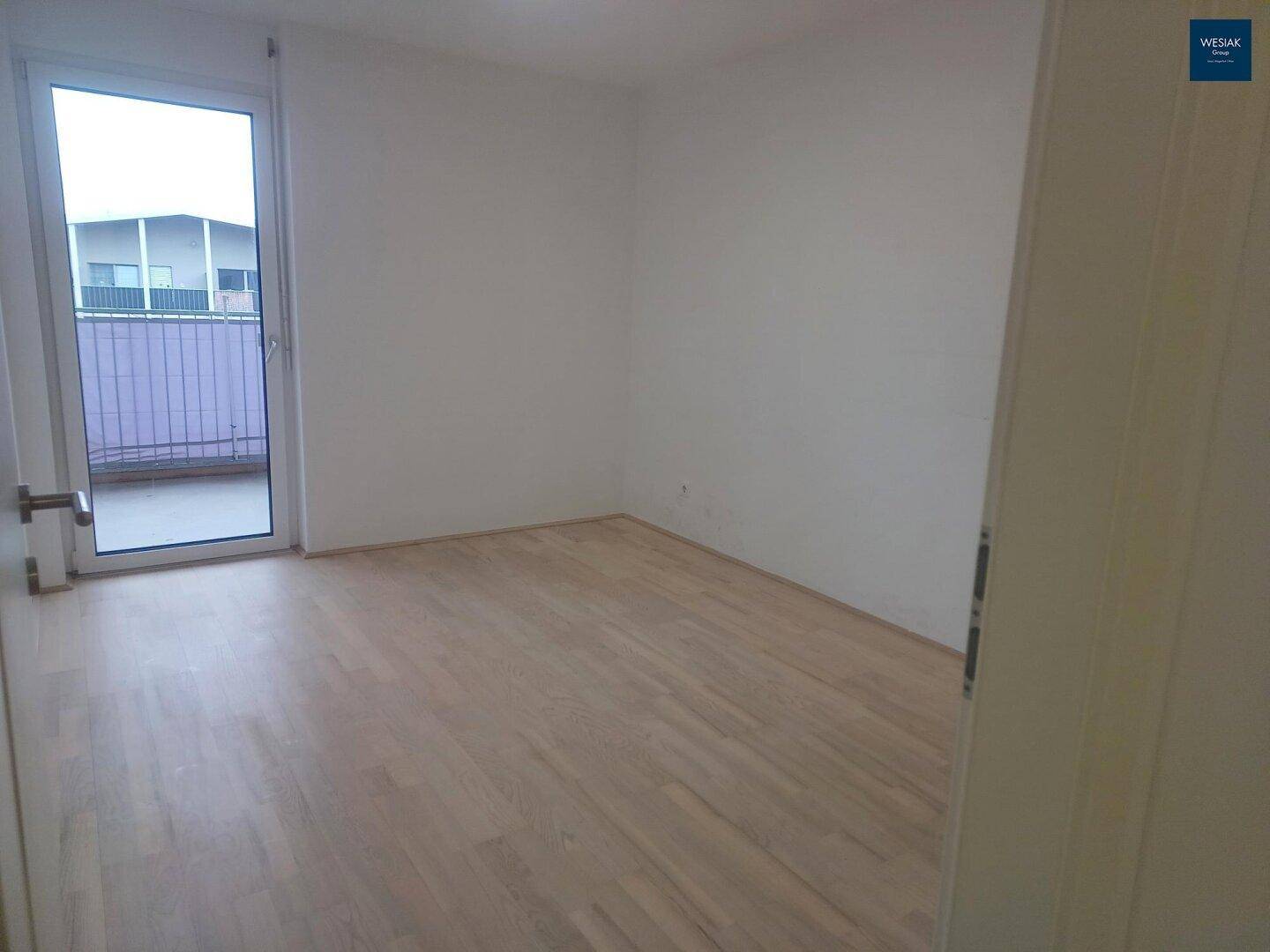 Helles Schlafzimmer mit Holzboden und Zugang zu einem kleinen Balkon.