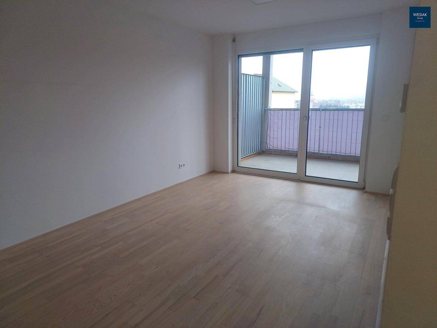 Heller Wohnbereich mit Holzboden und breiter Schiebetür zum Balkon.