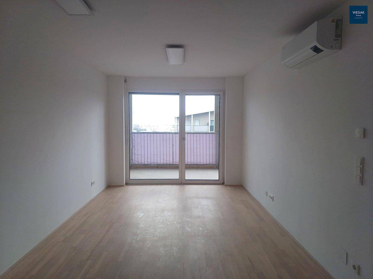 Lichtdurchfluteter Wohnraum mit Holzboden, Klimaanlage und Zugang zum Balkon.