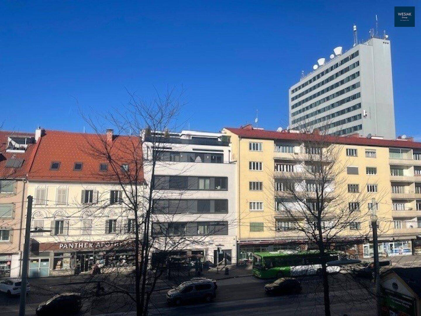 Stadtansicht mit verschiedenen Gebäuden, Straßenverkehr und einem hohen Gebäude im Hintergrund.