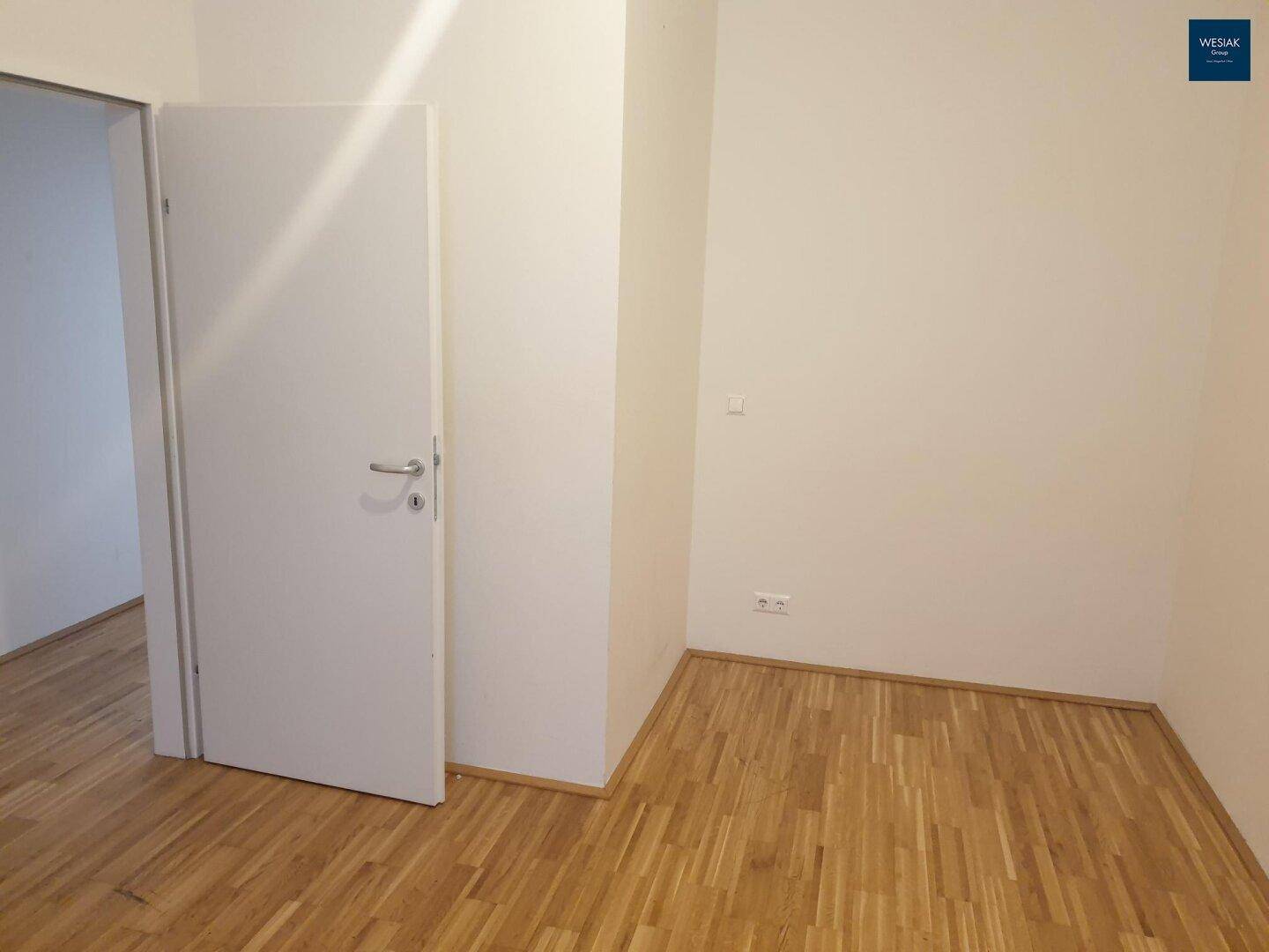 Leeres Zimmer mit Parkettboden und Tür, bereit zur individuellen Einrichtung.