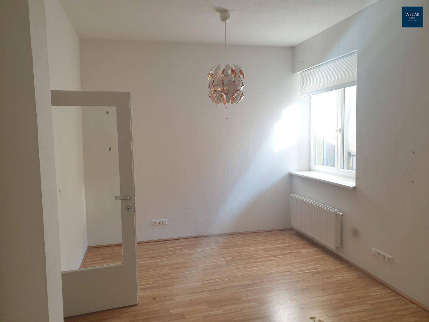 Helles Schlafzimmer mit Parkettboden, Fenster und moderner Deckenleuchte, bietet viel Tageslicht.