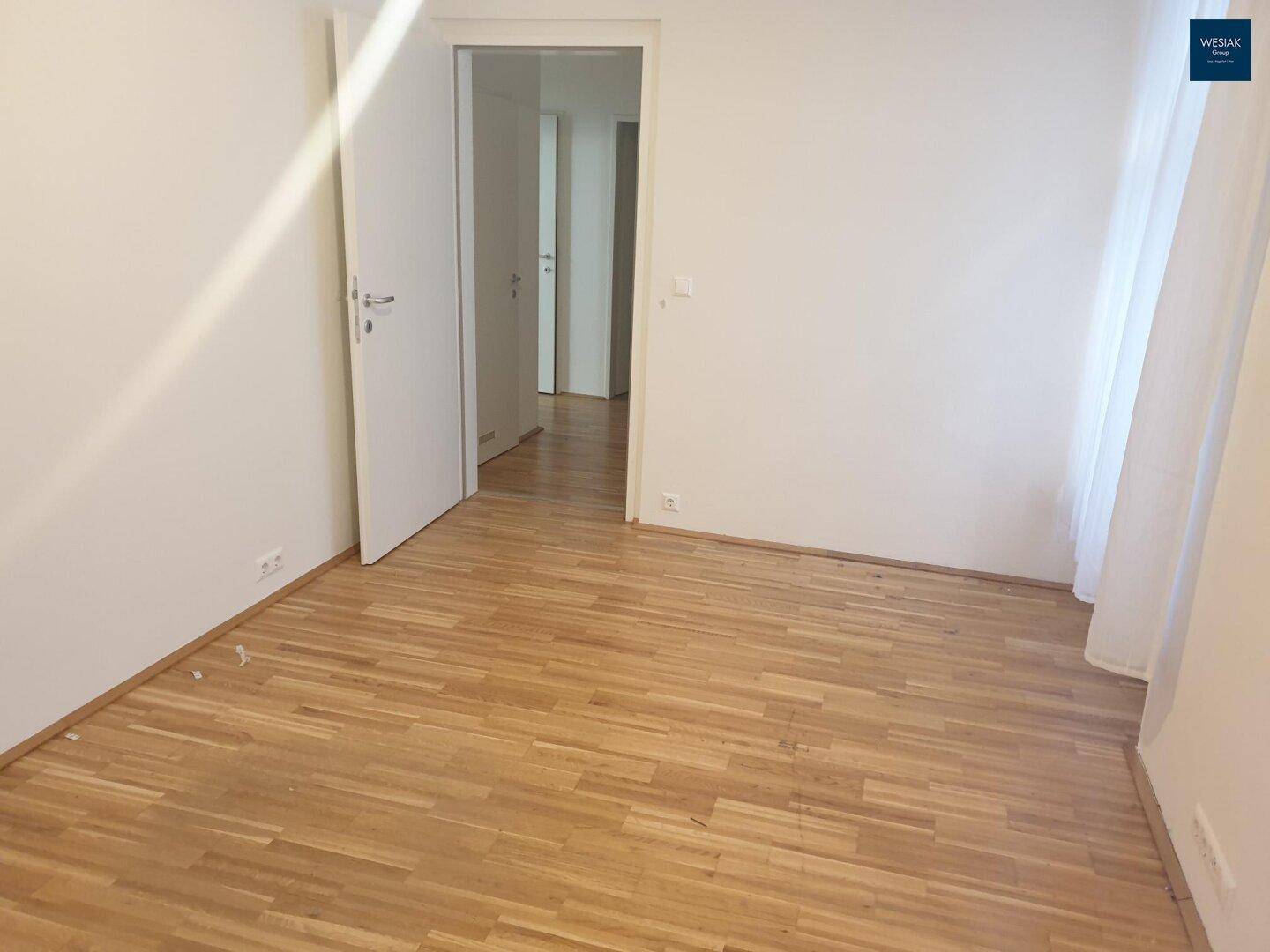 Leeres Zimmer mit Parkettboden und Zugang zu einem weiteren Raum, bietet flexible Nutzungsmöglichkeiten.