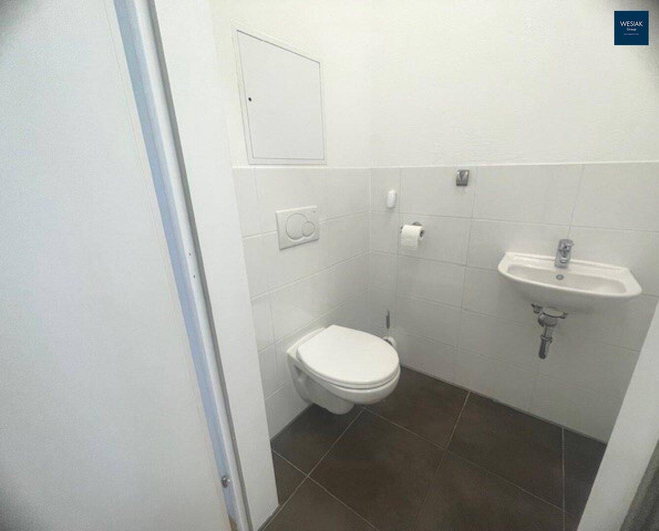 Modernes Gäste-WC mit Wand-WC und kleinem Waschbecken, weiß gefliest und funktional.