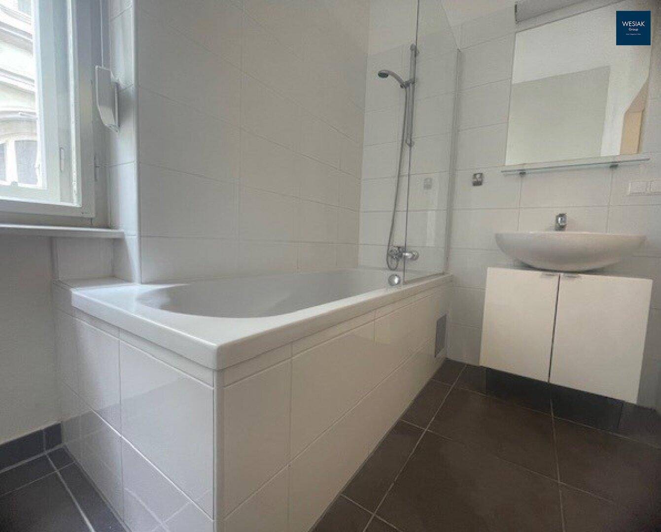 Helles Badezimmer mit Badewanne, Duschfunktion und modernem Waschbecken, inklusive Fenster.