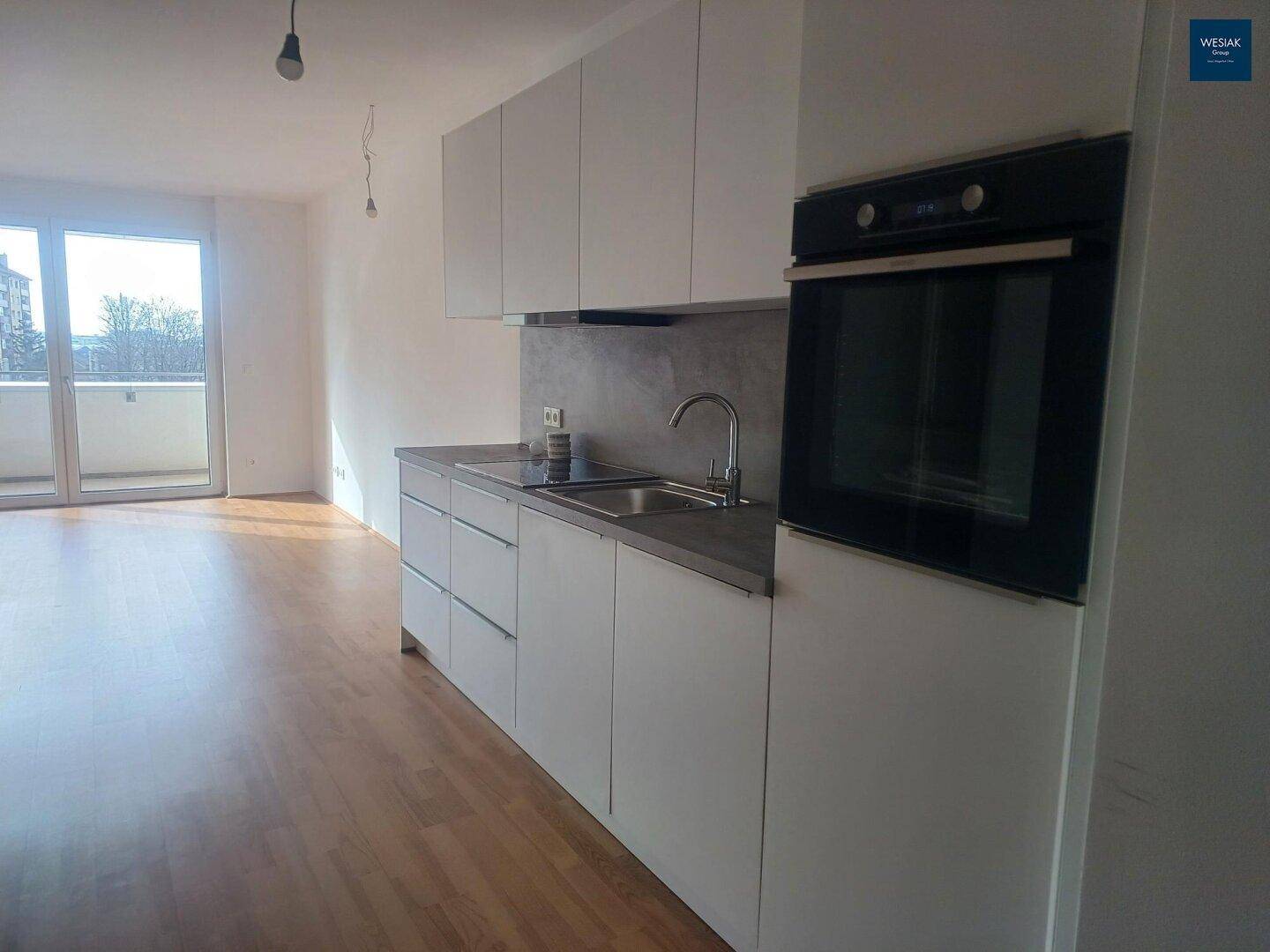 Moderne Küchenzeile mit weißen Schränken, integriertem Backofen und Blick auf den Balkon.