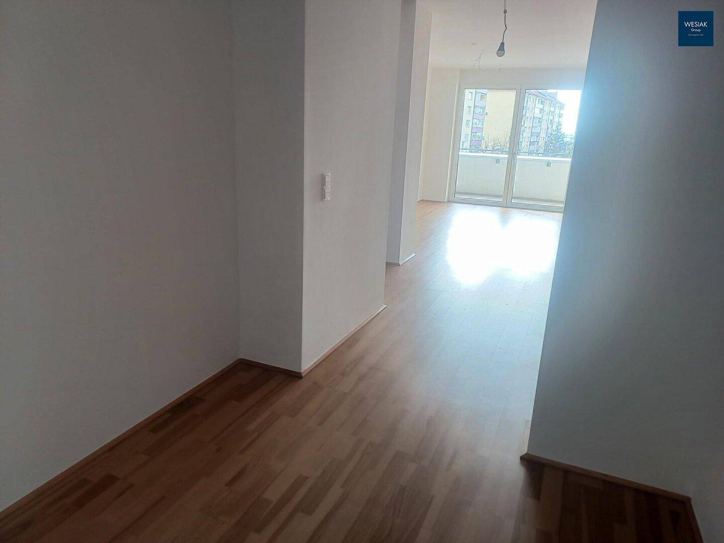 Heller Flur mit Holzparkettboden, der in einen lichtdurchfluteten Wohnbereich führt.