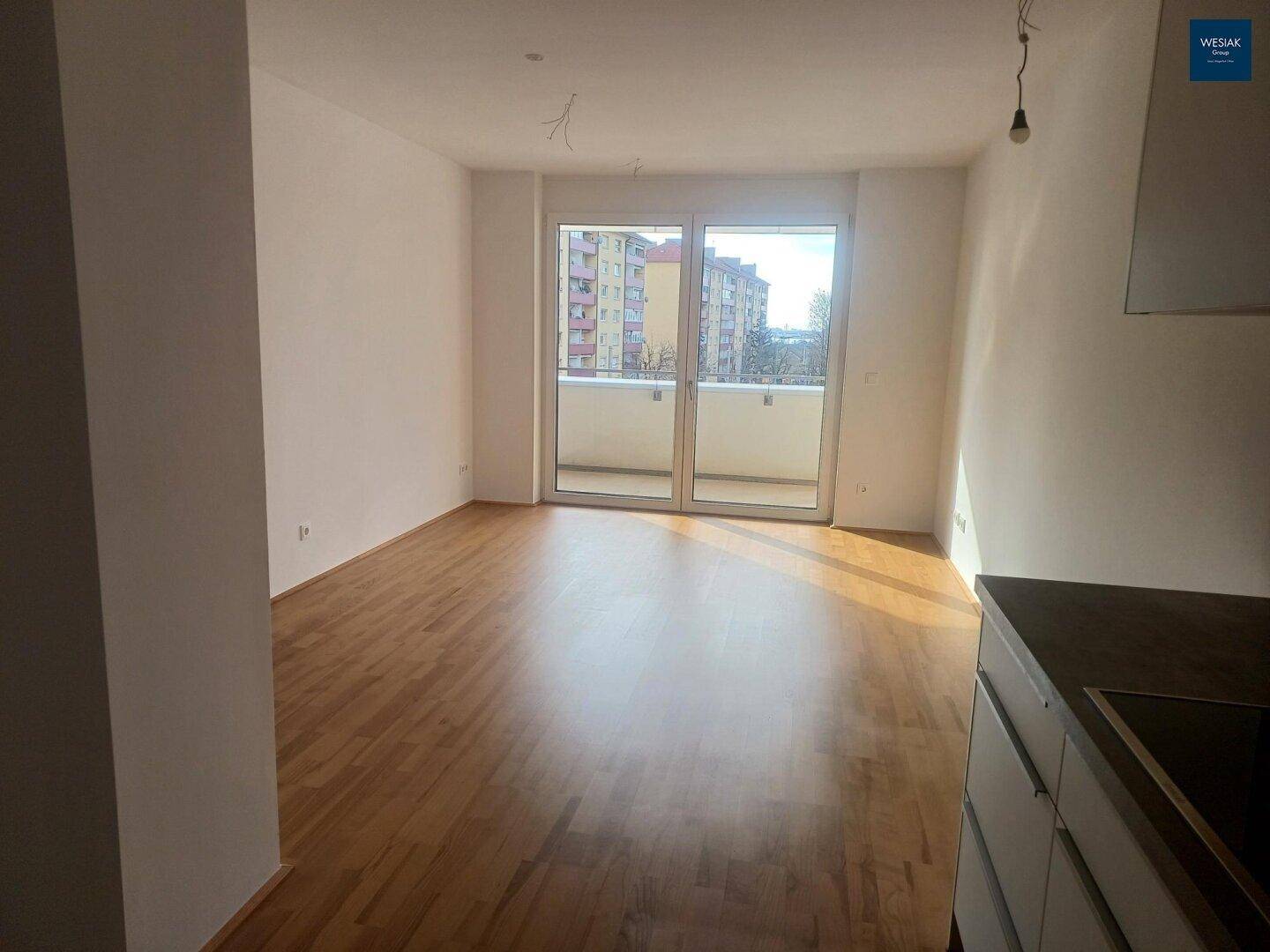 Lichtdurchfluteter Wohnbereich mit Holzboden und großem Balkonzugang, der viel Tageslicht hereinlässt.