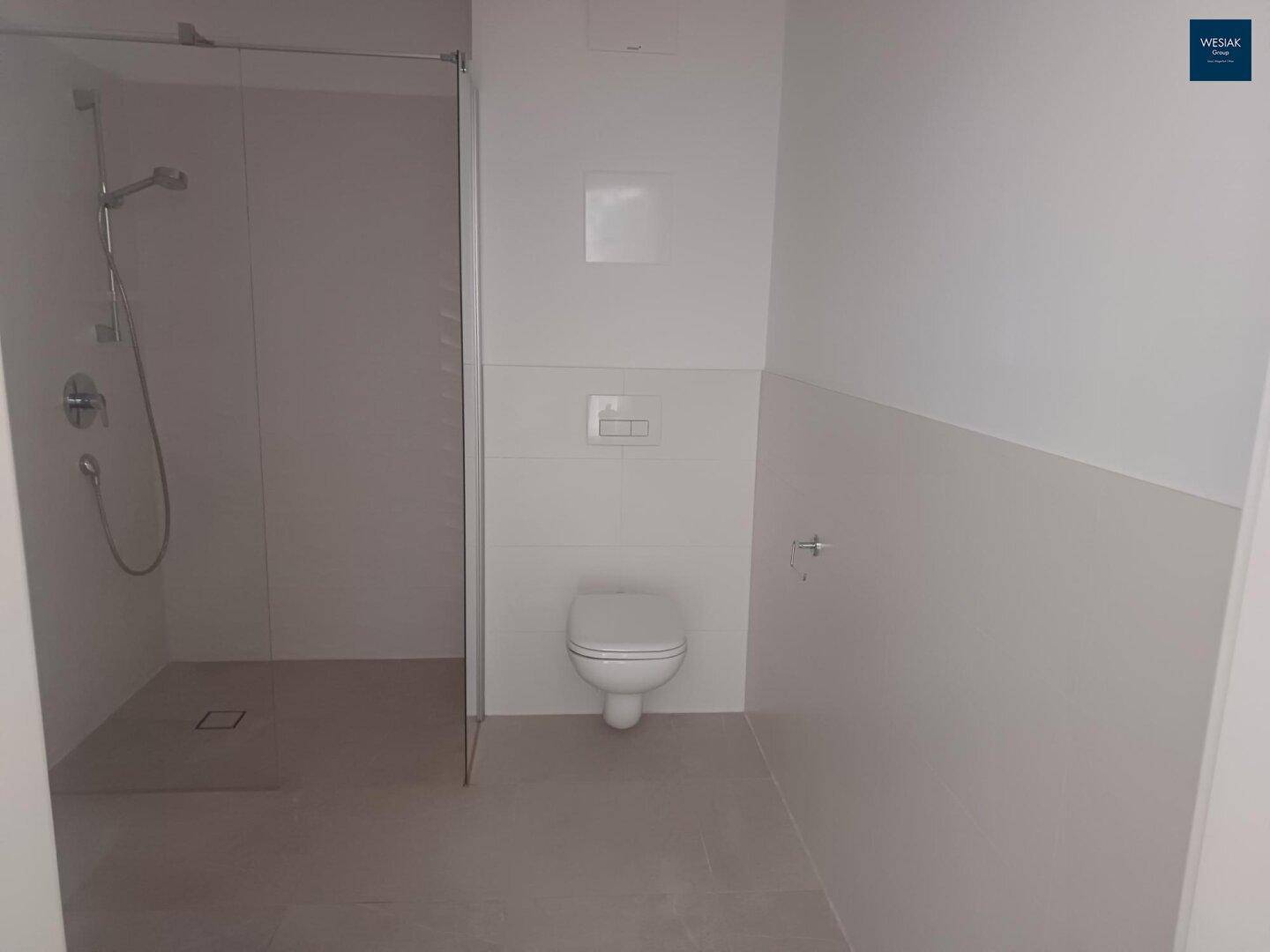 Modernes Badezimmer mit ebenerdiger Dusche und wandhängendem WC in hellen Fliesen.