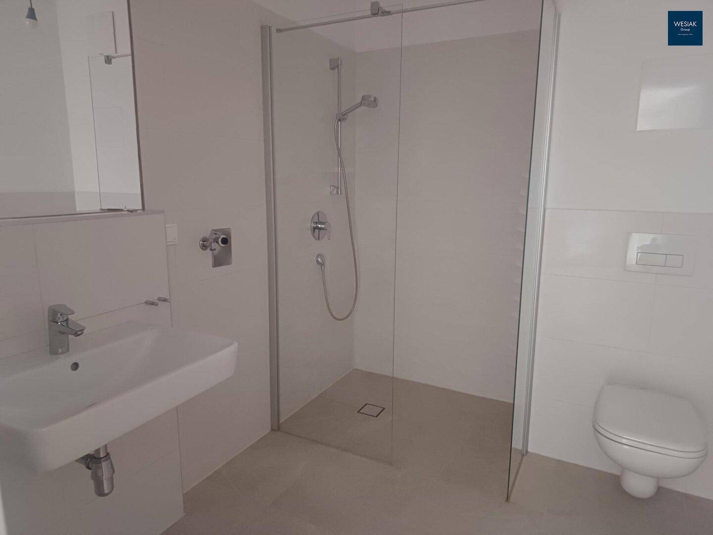 Helles Badezimmer mit Waschbecken, ebenerdiger Dusche und wandhängendem WC.