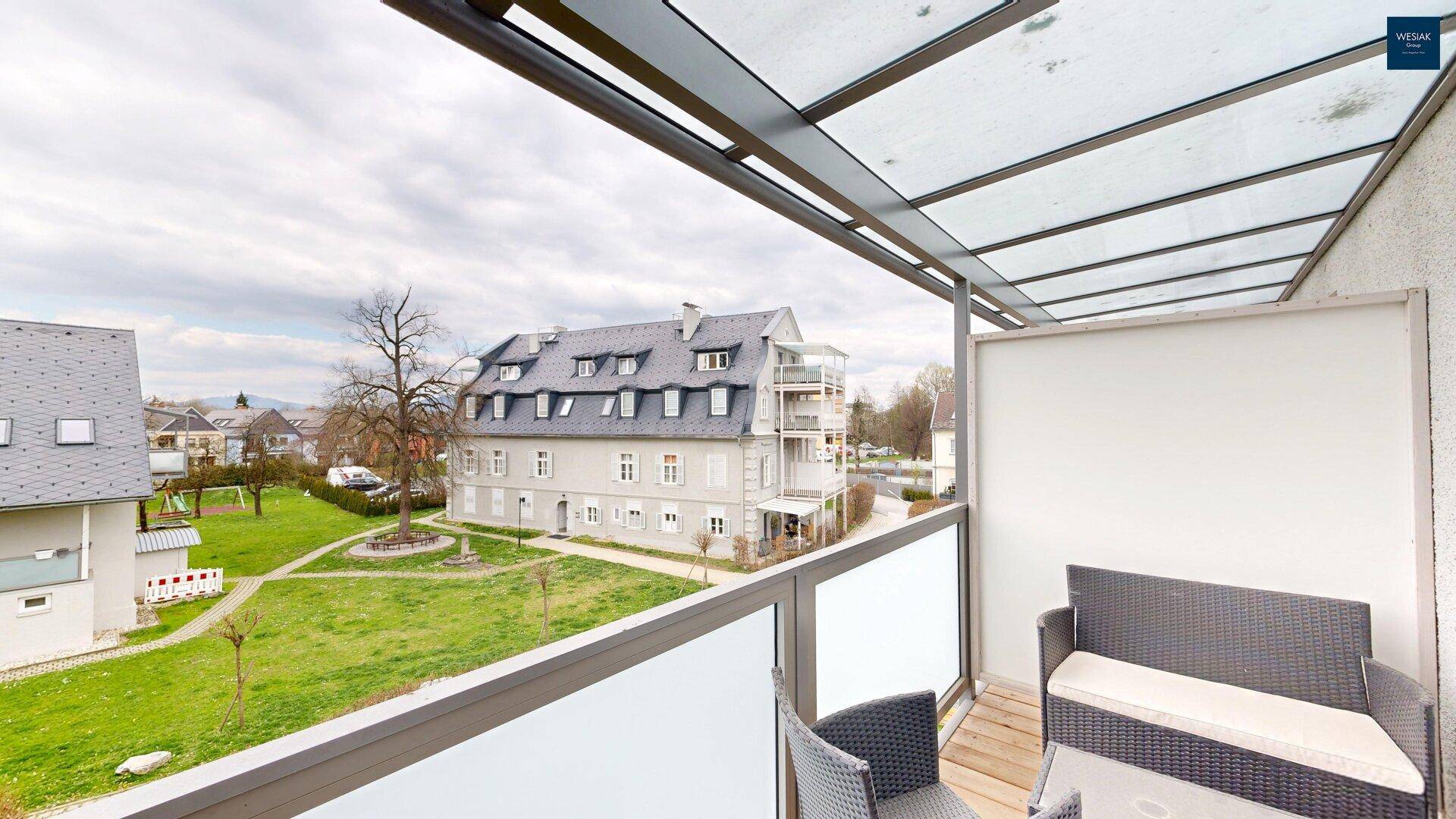 Balkon mit Sitzgelegenheiten und weitem Blick über die grüne Umgebung und Gebäude.