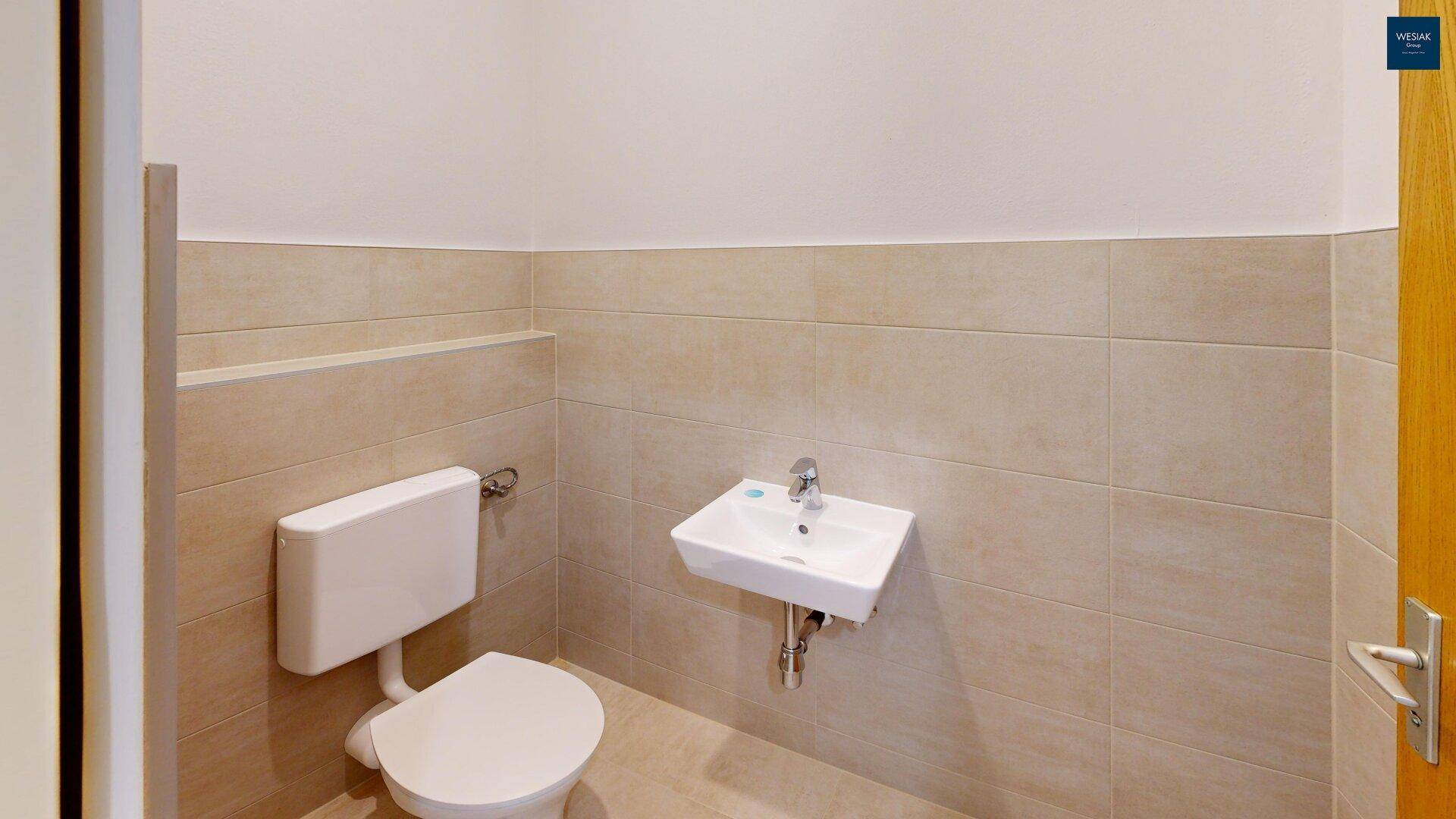 Schlichte Gästetoilette mit WC und Waschbecken, gefliest in hellen Farbtönen.