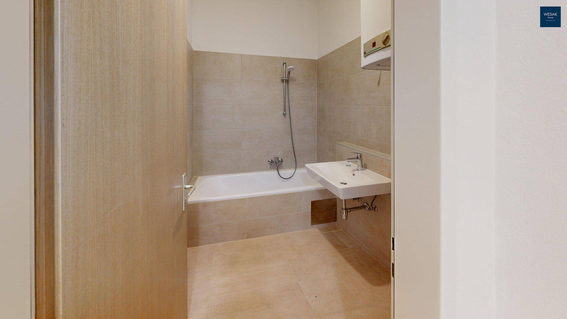 Helles Badezimmer mit Badewanne, Waschbecken und beigefarbenen Wandfliesen.