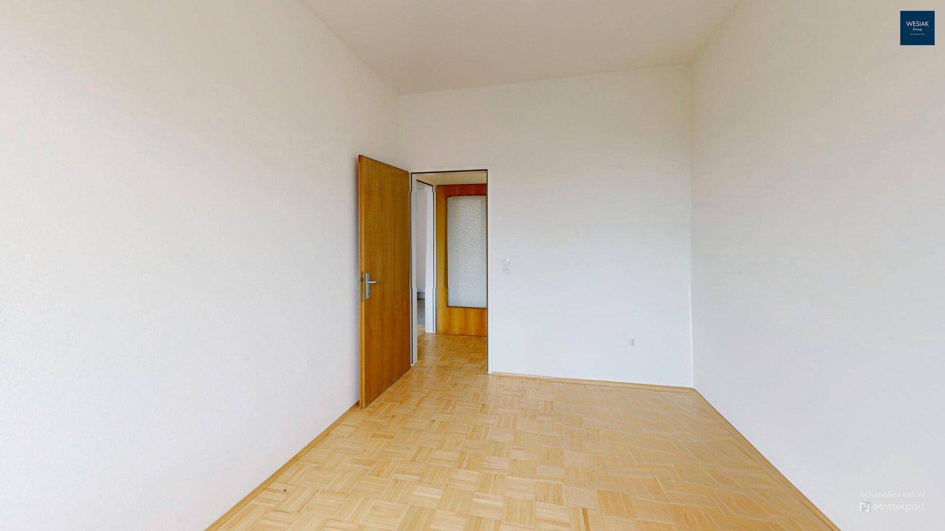 Leeres Schlafzimmer mit Parkettboden und Holztür.