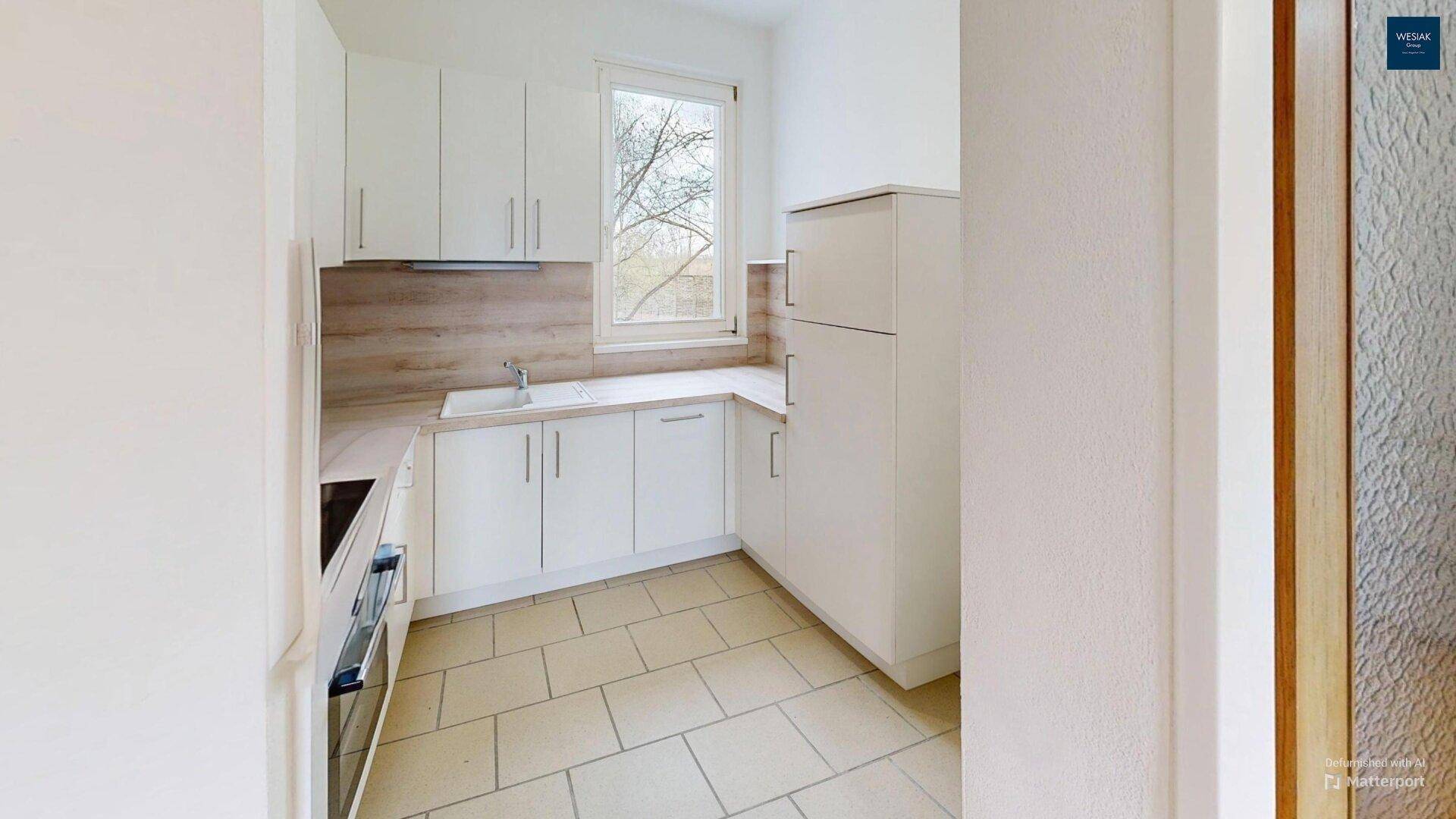 Leere Küche mit weißen Schränken, Fliesenboden und Fenster.