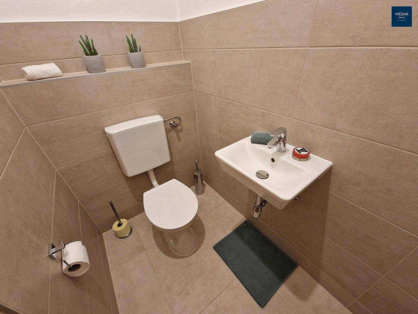 Separate Gästetoilette mit WC, kleinem Waschbecken und beigefarbenen Fliesen.