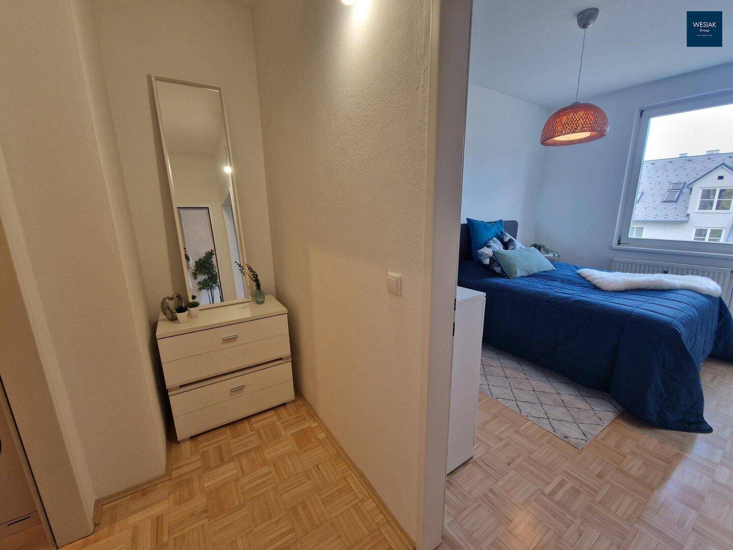 Flur mit Kommode, Spiegel und Blick in ein helles Schlafzimmer.