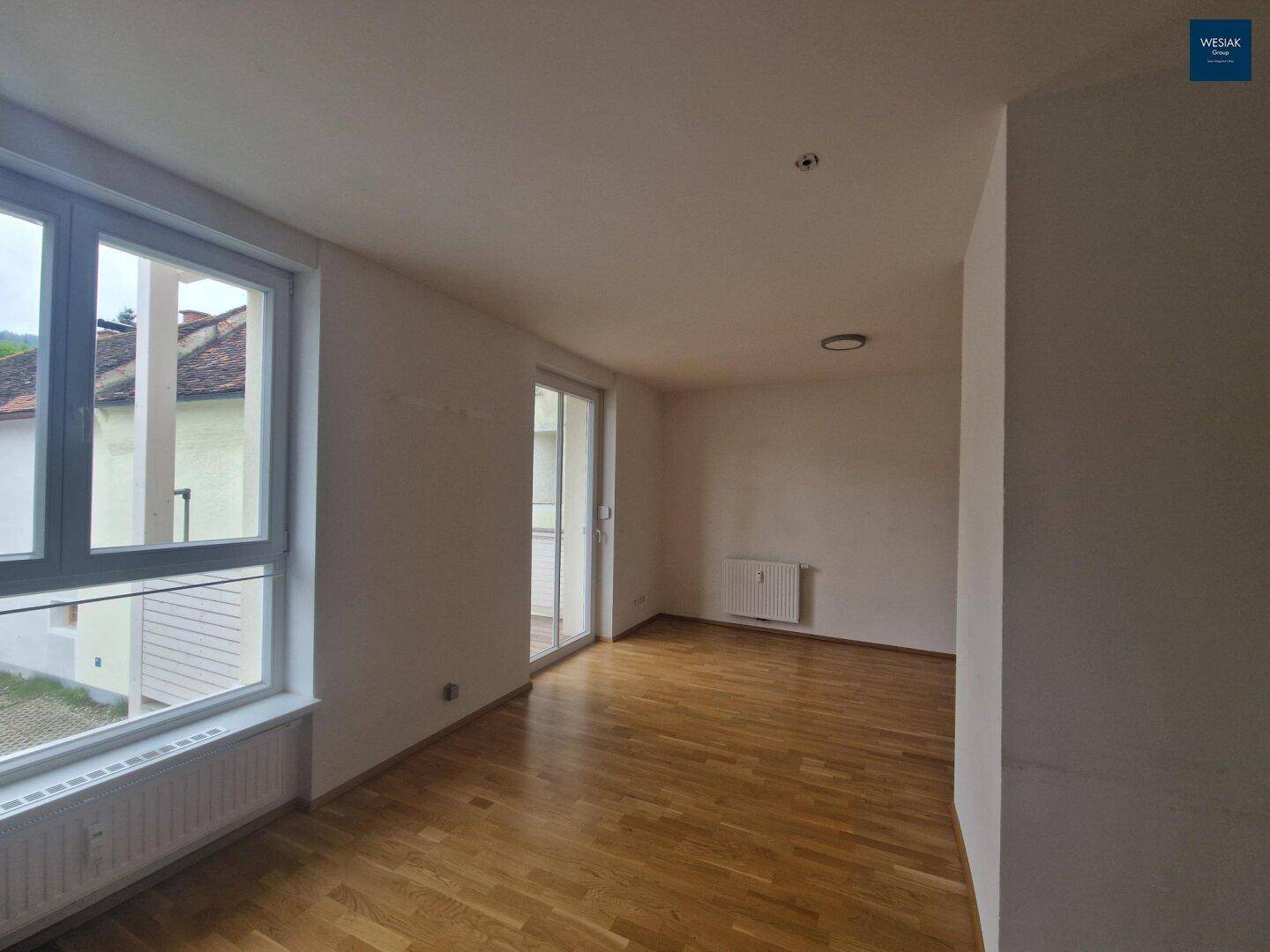 Geräumiges Wohnzimmer mit Parkettboden, großen Fenstern und Zugang zu einem Balkon.
