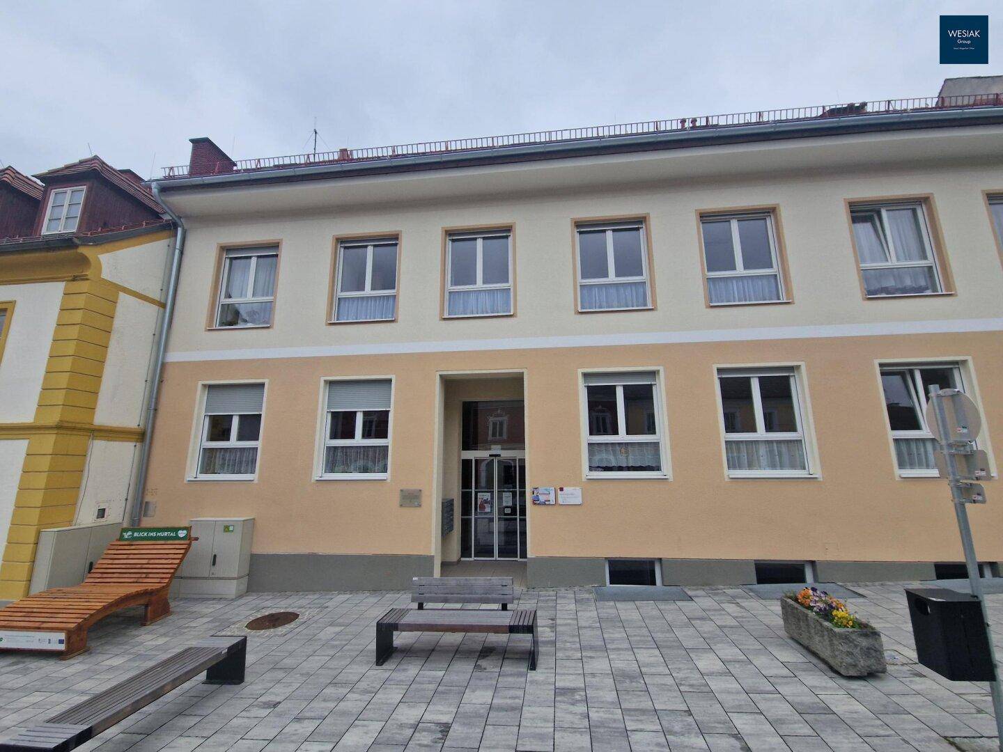Vorderansicht des Gebäudes mit Eingangsbereich und gepflastertem Vorplatz.
