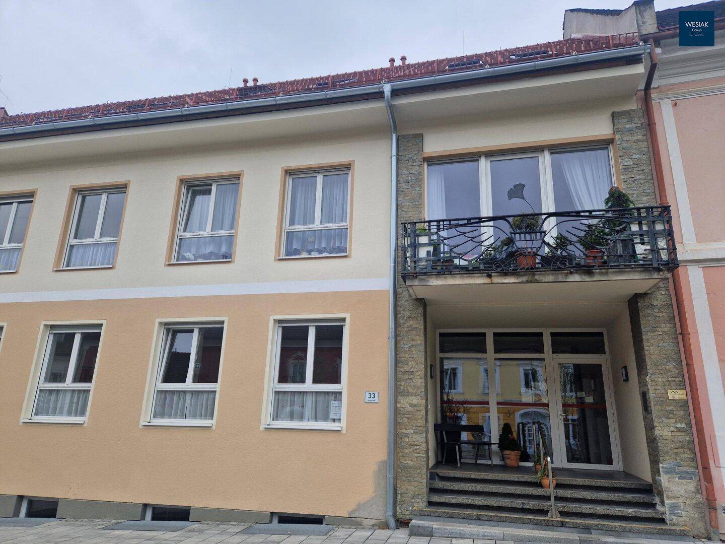 Gebäudefassade mit Eingangsbereich und einem Balkon mit dekorativem Geländer.