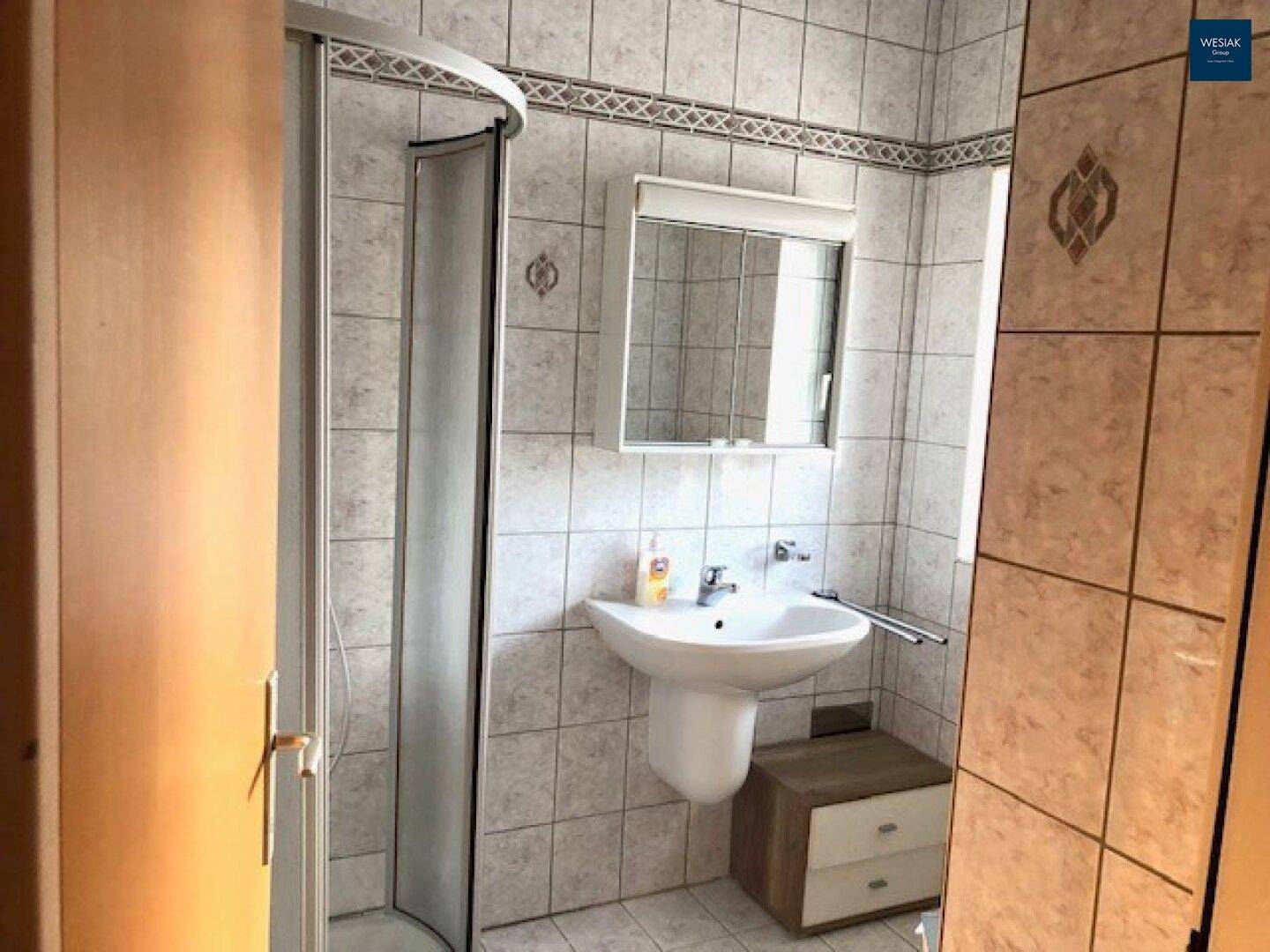 Badezimmer mit Duschkabine, Waschbecken und hellen Fliesen an Wänden und Boden.