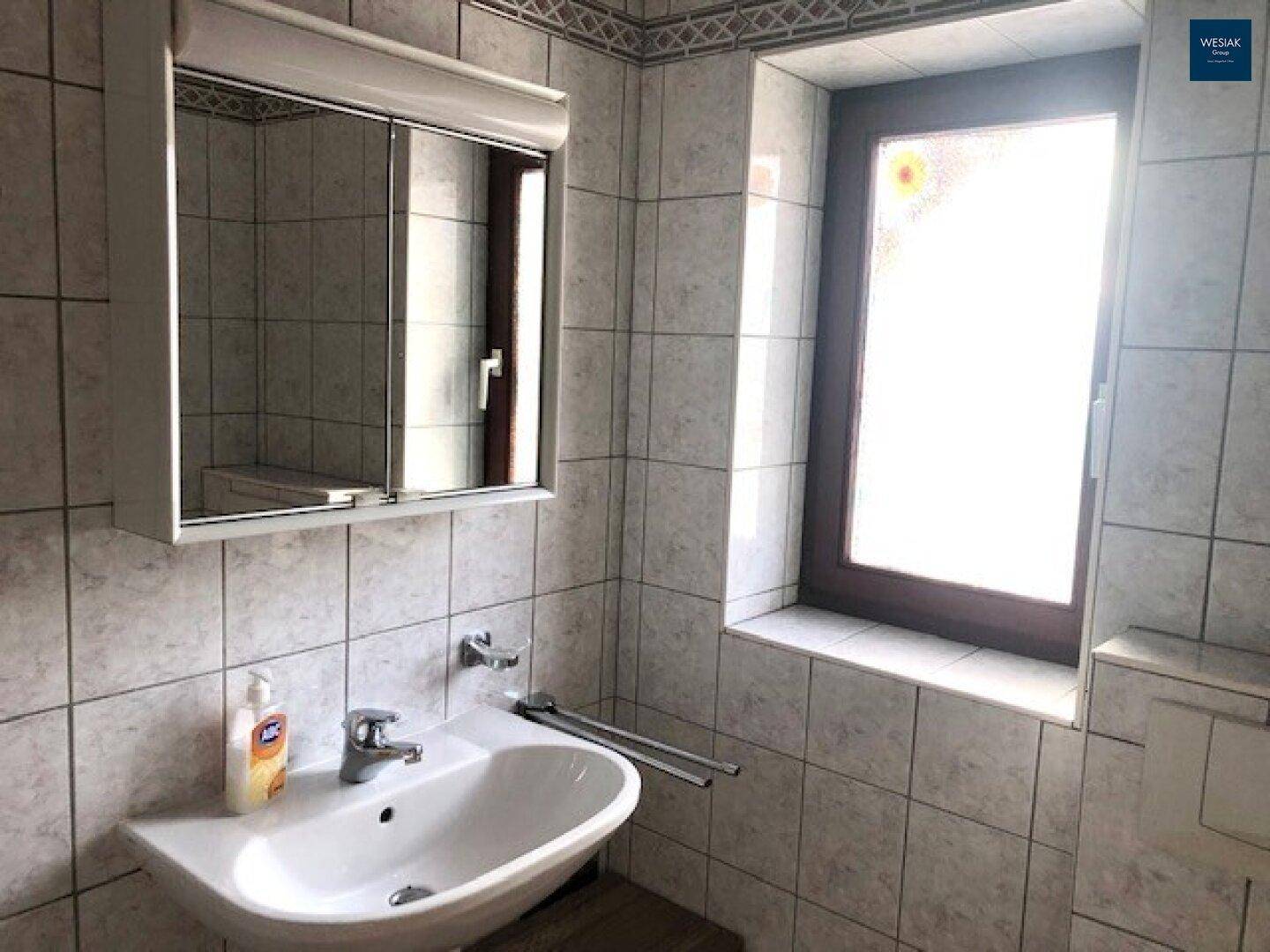 Helles Badezimmer mit Waschbecken, Spiegelschrank und Fenster für Tageslicht.