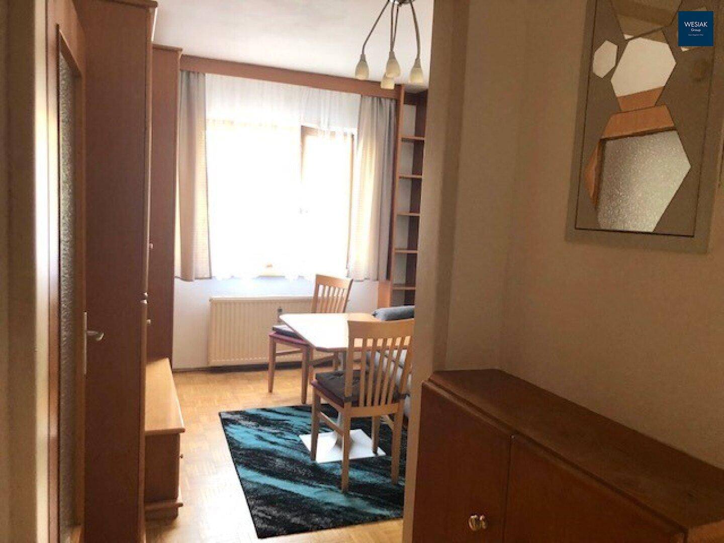 Gemütlicher Wohnbereich mit Holzmöbeln, Parkettboden und Blick zum Fenster.