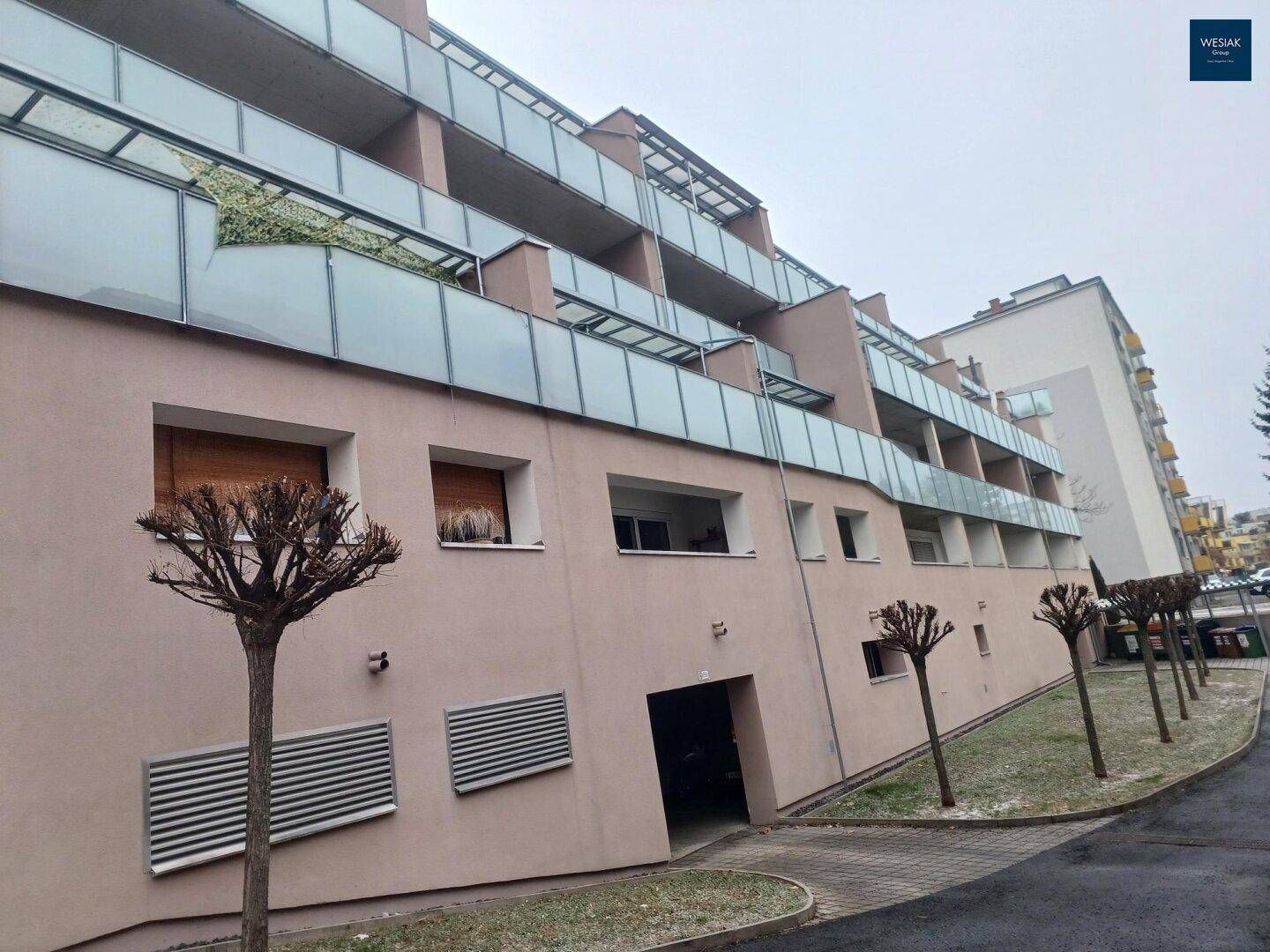 Mehrstöckiges Wohngebäude mit zahlreichen Balkonen und moderner Glasfassade unter bewölktem Himmel.