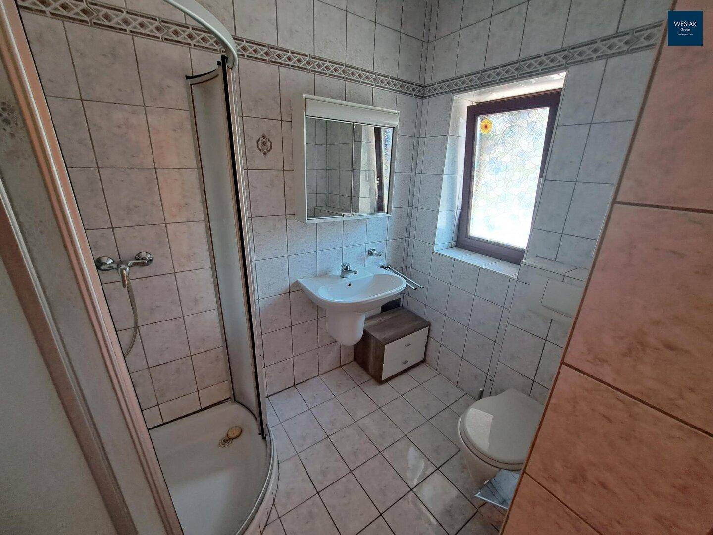 Badezimmer mit Duschkabine, Waschbecken, WC und Fenster für natürliche Belüftung.