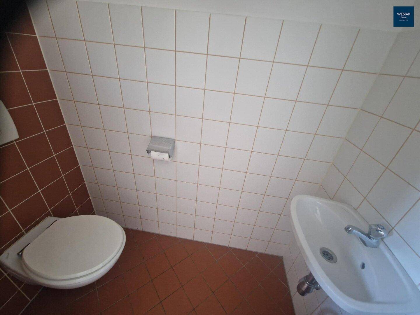 Kleines Gäste-WC mit Fliesenboden, Toilette und Waschbecken, in schlichtem Design.