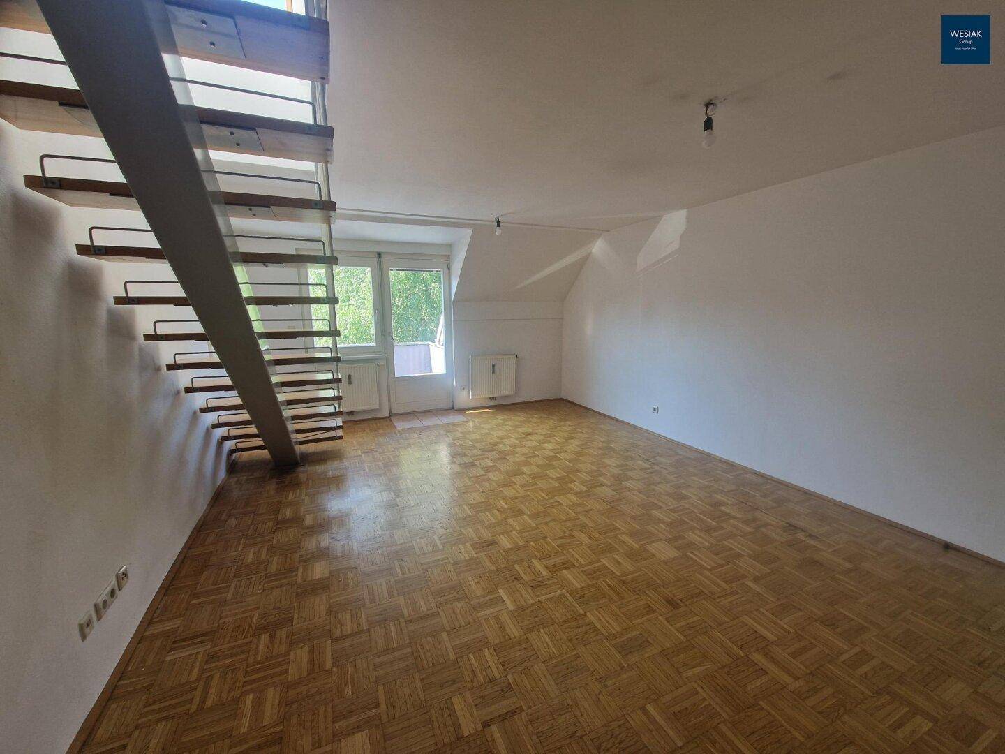 Geräumiges Wohnzimmer mit Parkettboden und offener Treppe zum Obergeschoss, mit Balkonzugang.
