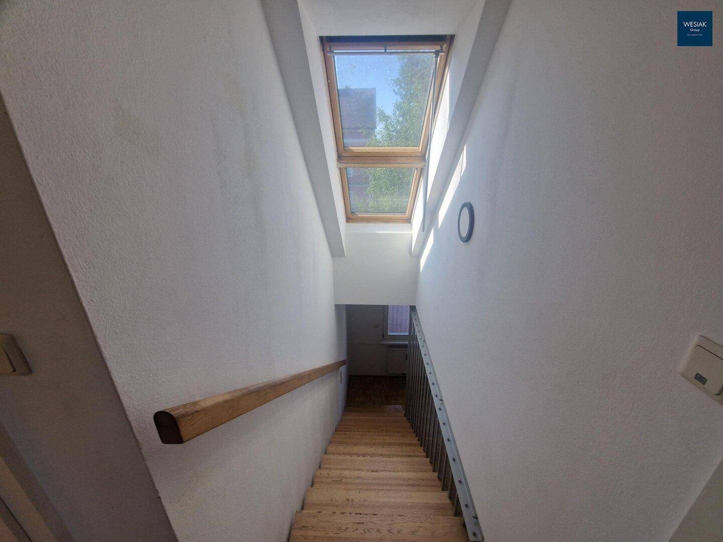 Helles Treppenhaus mit Holzstufen, Geländer und Oberlichtern für viel Tageslicht.