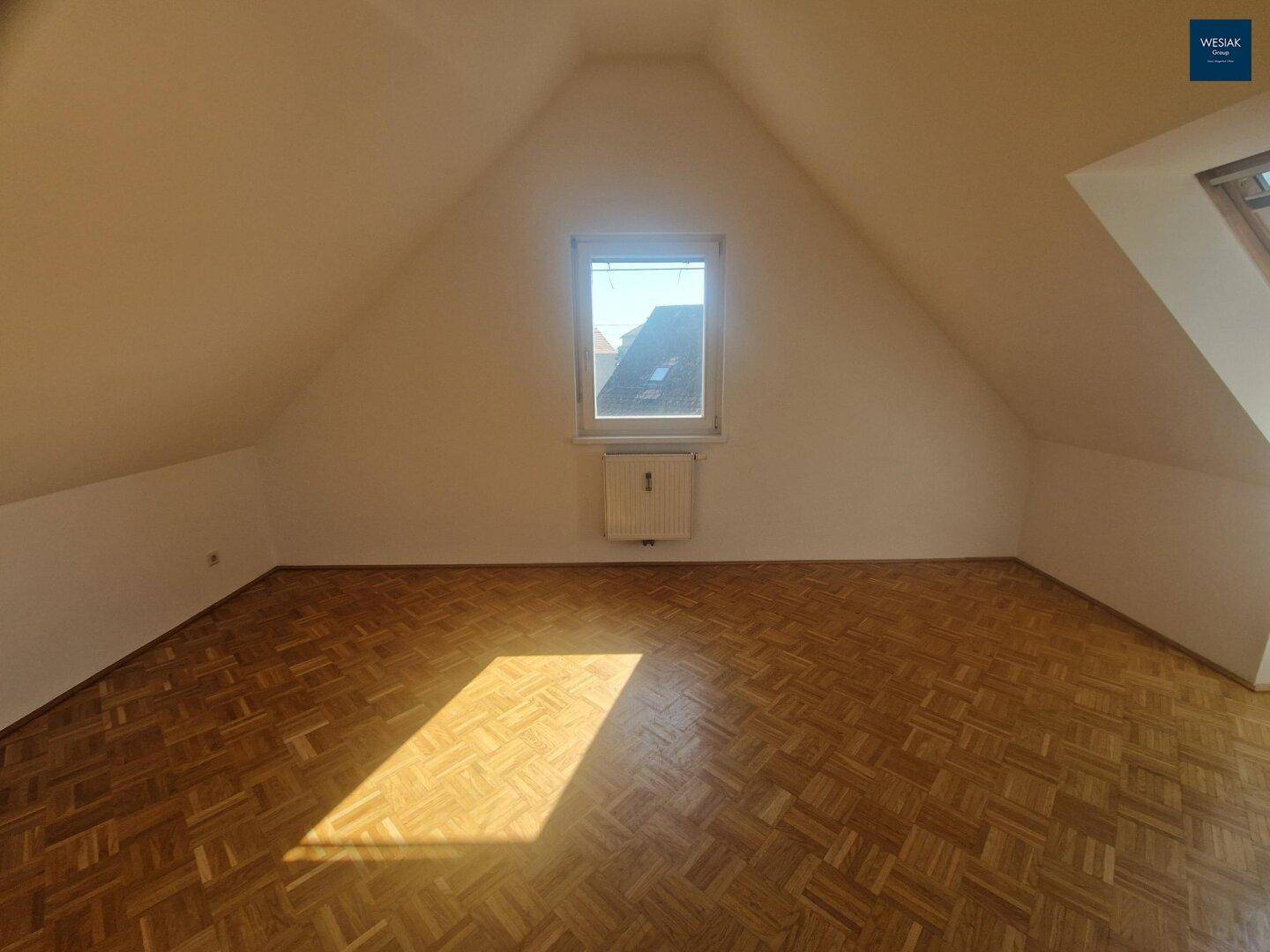 Heller Dachgeschossraum mit Parkettboden und Fenster mit Blick nach draußen, unmöbliert.