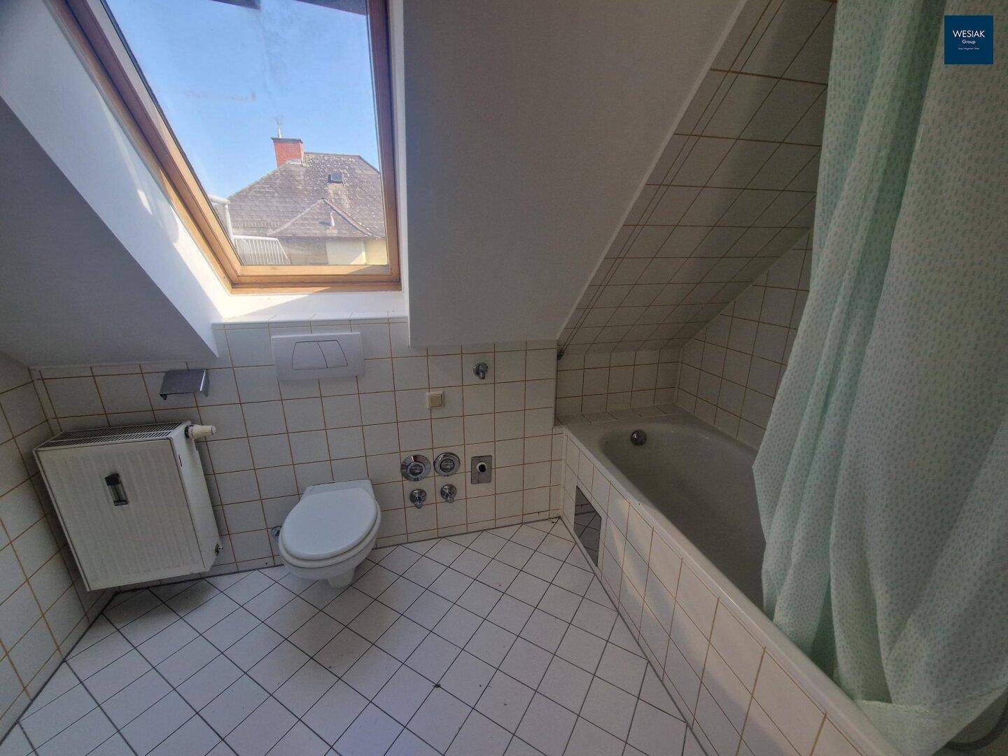 Badezimmer im Dachgeschoss mit Badewanne, WC, weißen Fliesen und Dachfenster.