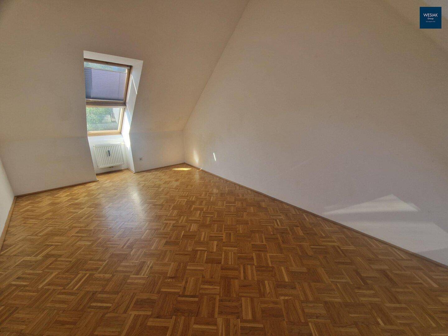 Heller Dachgeschossraum mit Parkettboden und Dachfenster, unmöbliert und sonnendurchflutet.