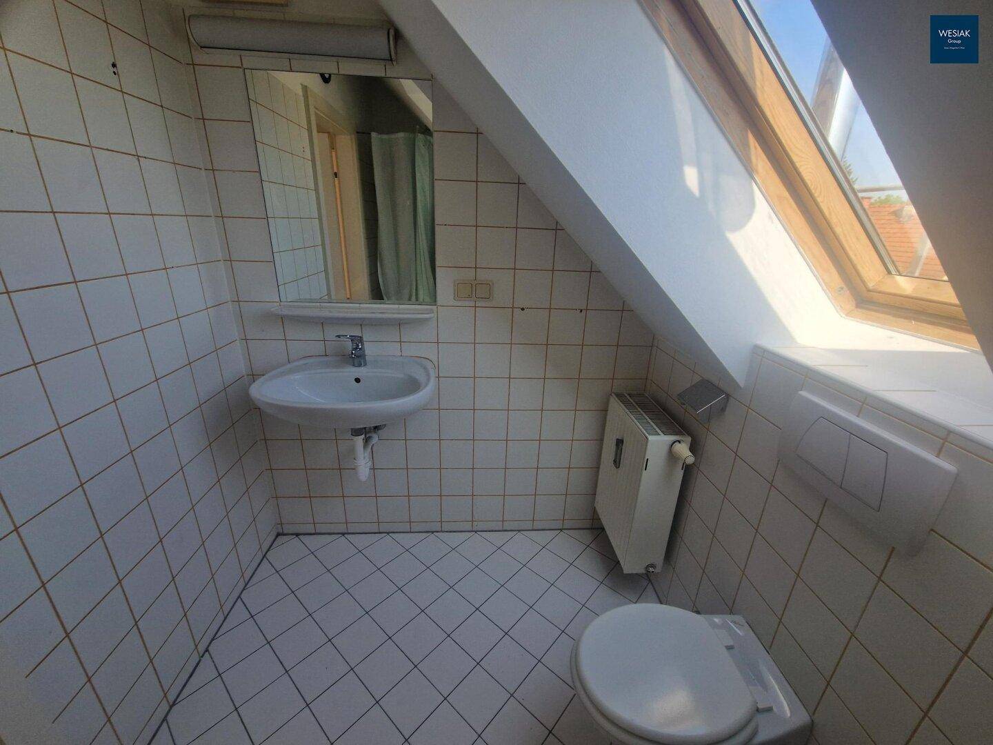 Badezimmer im Dachgeschoss mit weißen Fliesen, Waschbecken, WC und Dachfenster.