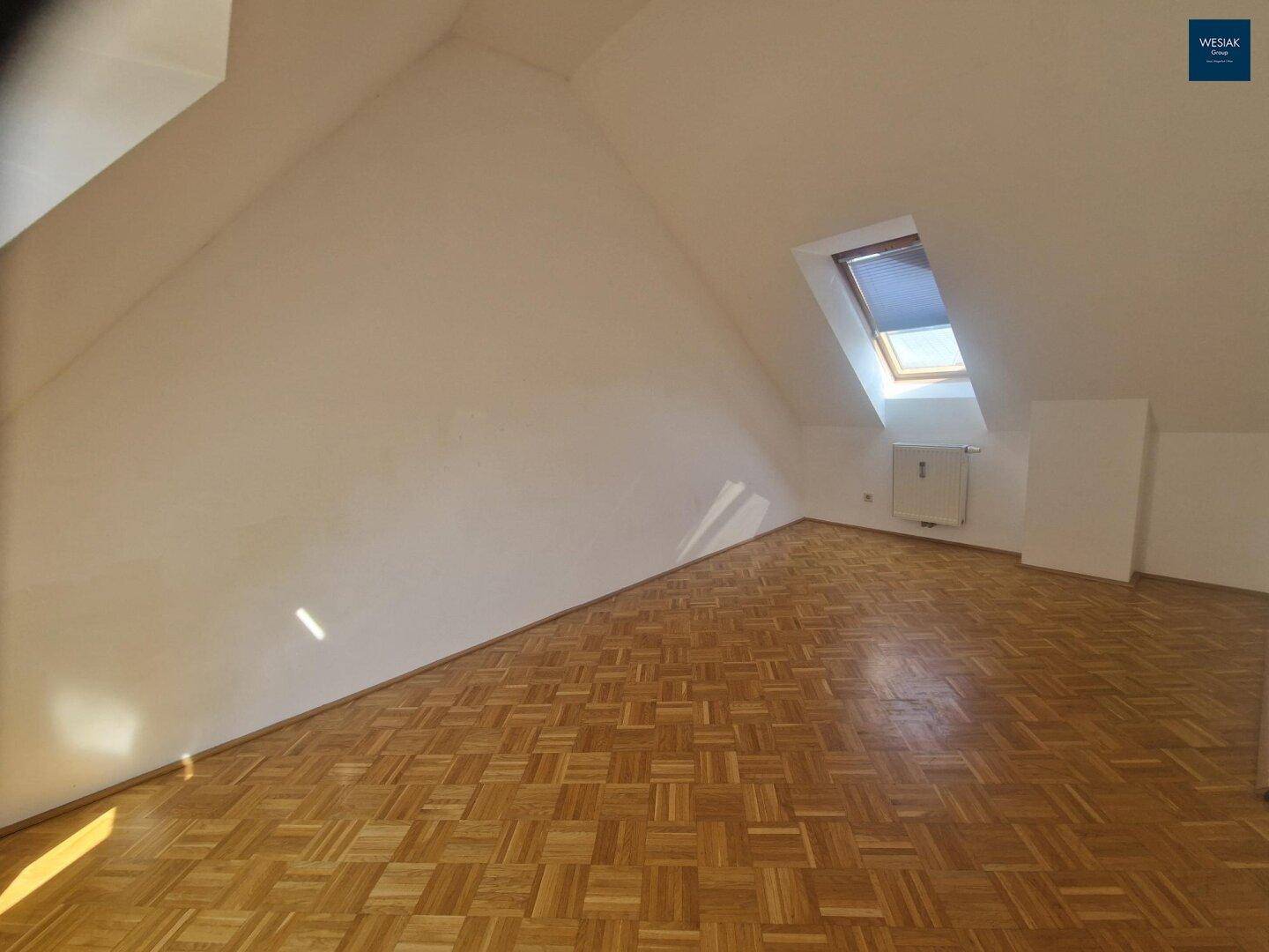 Geräumiger Dachgeschossraum mit Parkettboden und einem Dachfenster, unmöbliert.