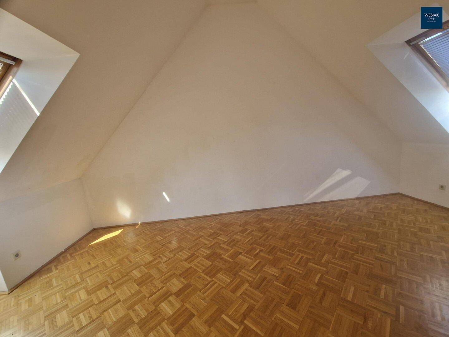 Heller Raum im Dachgeschoss mit Parkettboden und zwei Dachfenstern, unmöbliert.