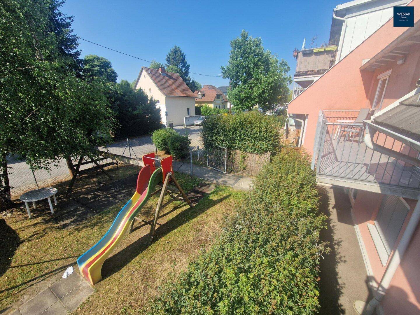 Gemeinschaftsgarten mit Spielplatz, Rutsche und viel Grünfläche, ideal für Familien.