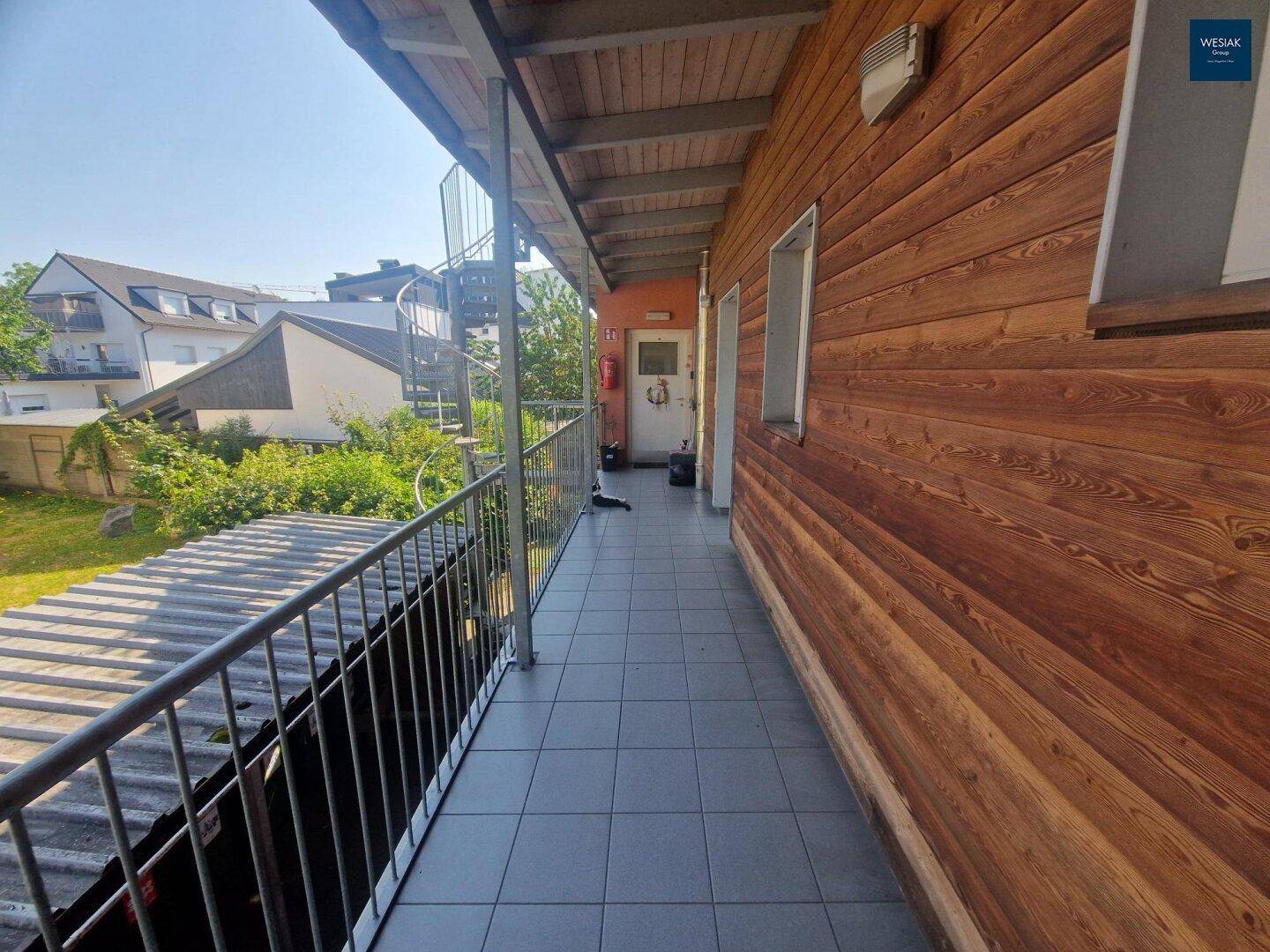 Langer Balkon mit Holzverkleidung, Fliesenboden und Blick auf die Umgebung.