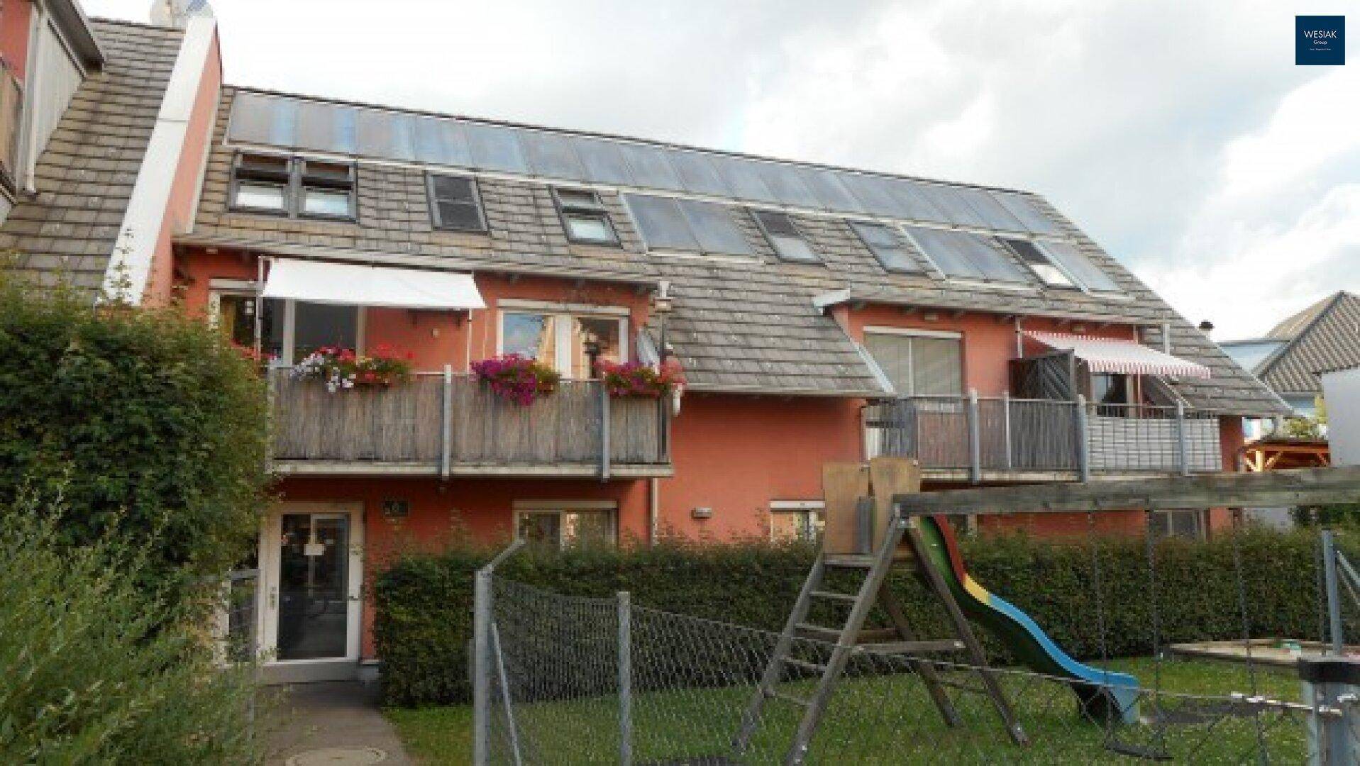 Gebäudefassade mit Solaranlage auf dem Dach und Spielplatz im Gartenbereich.