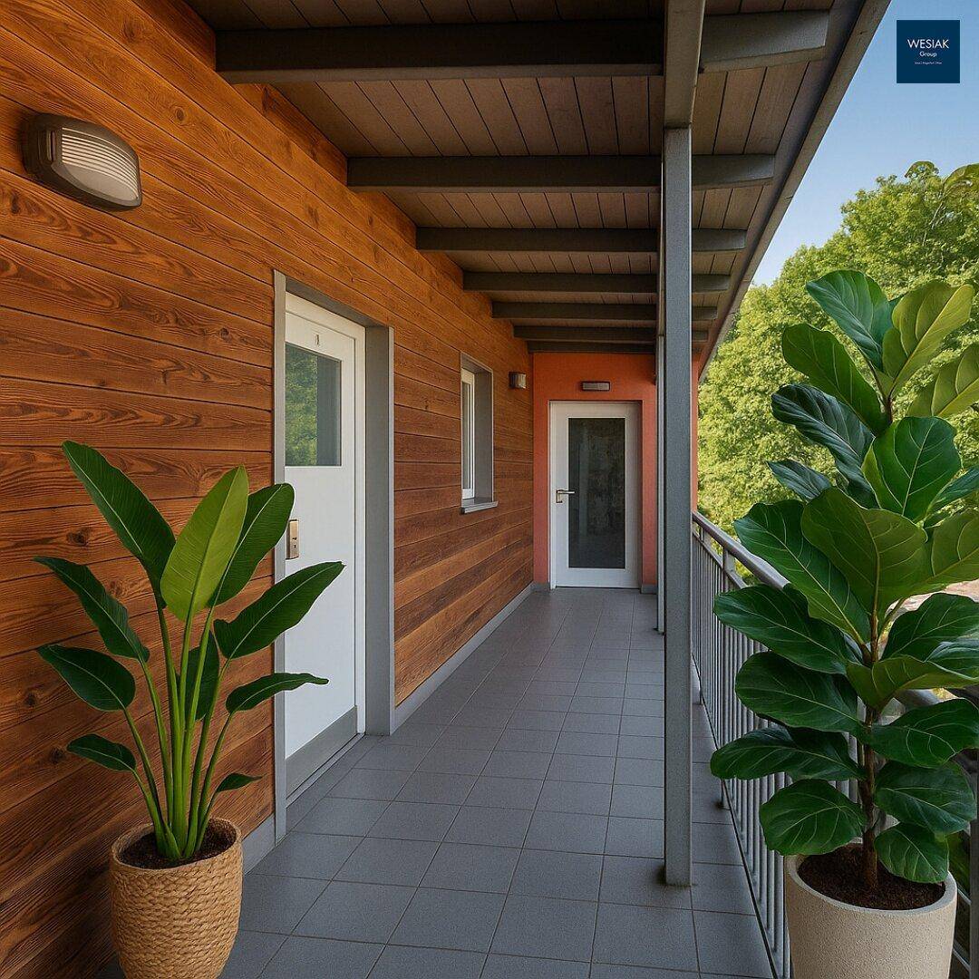 Langer Balkon mit Holzverkleidung, Fliesenboden und Blick ins Grüne.