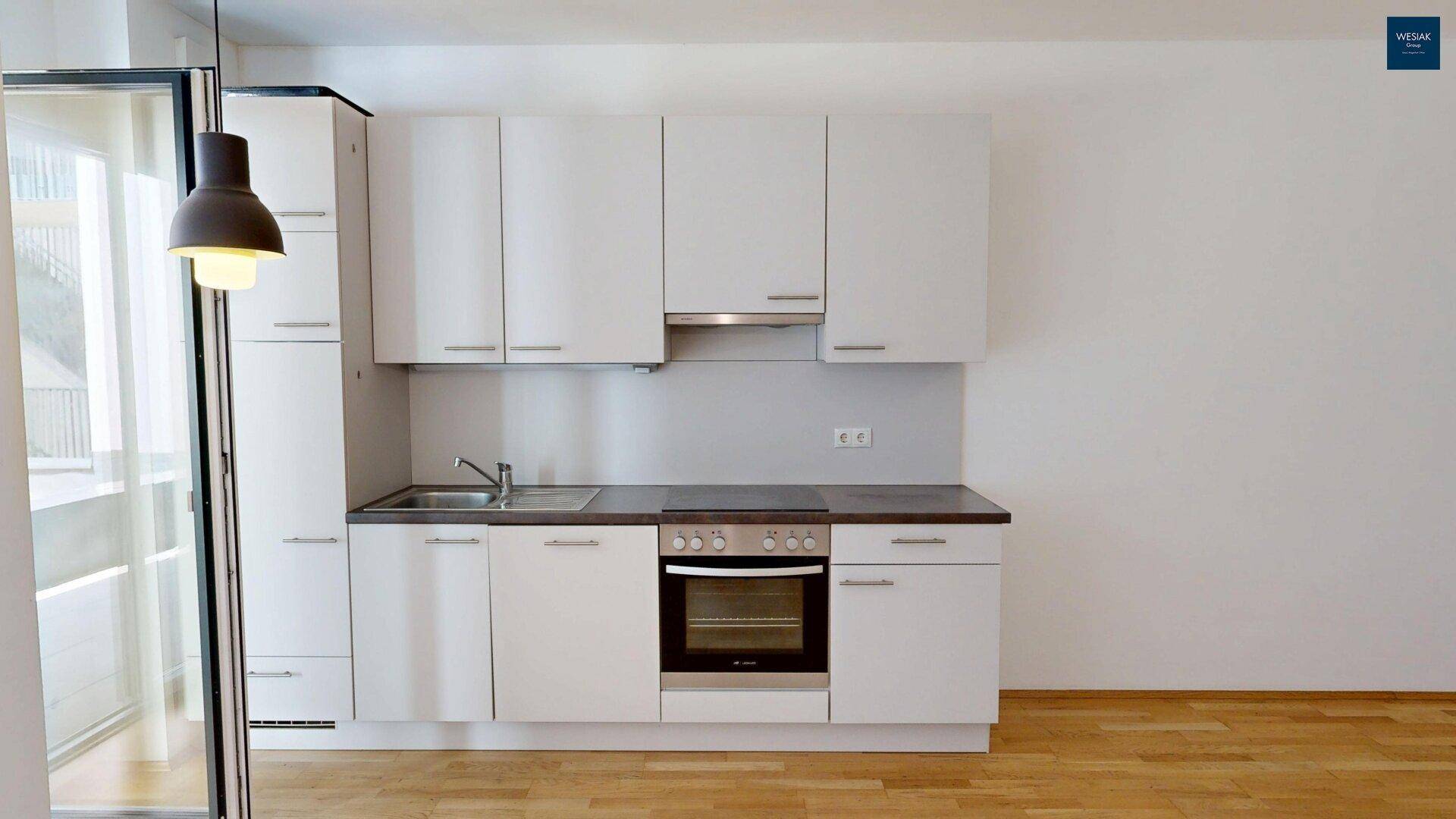 Moderne Küchenzeile mit weißen Fronten, integriertem Backofen und Dunstabzugshaube.