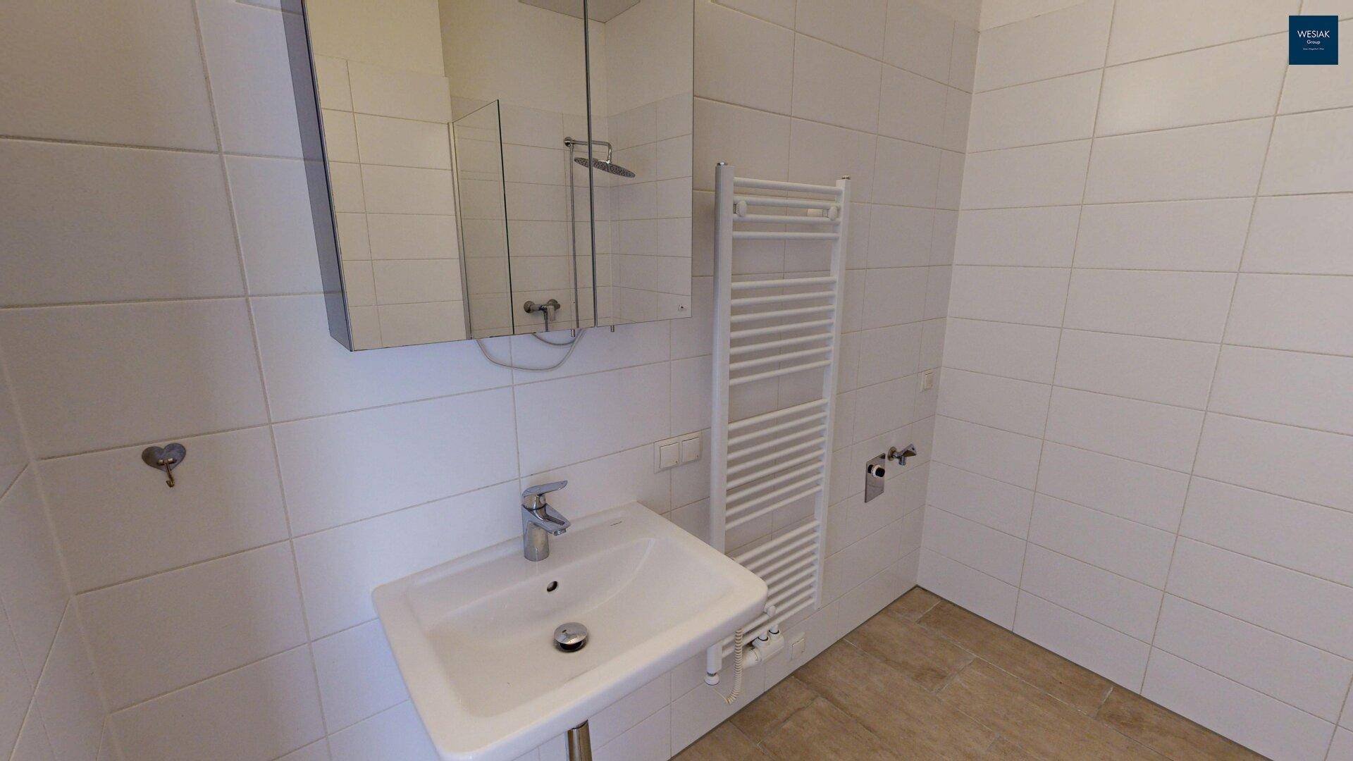 Modernes Badezimmer mit weißen Fliesen, Einzelwaschbecken und beheiztem Handtuchhalter.